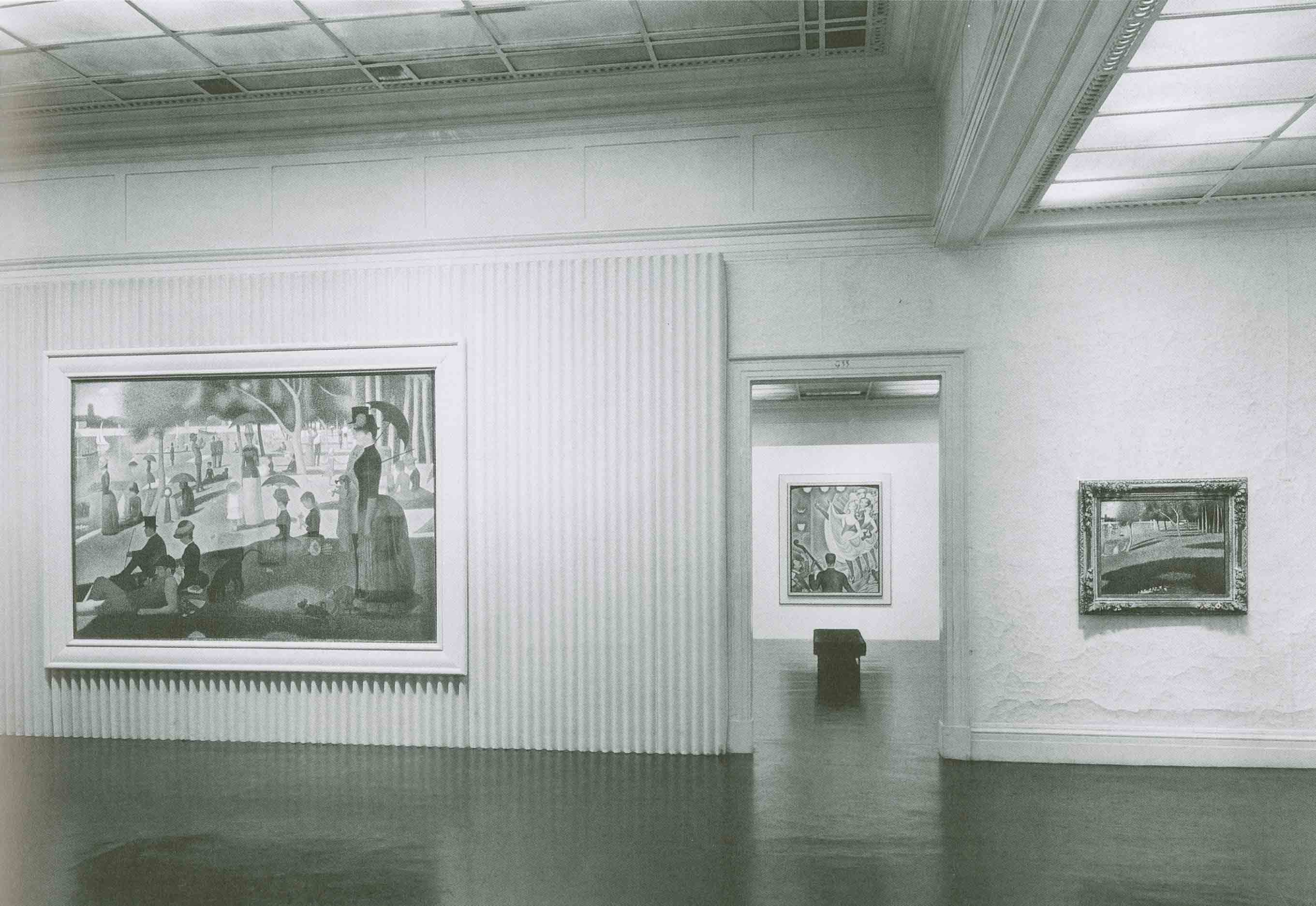 Black-and-white photograph of a stark, modern gallery space with corrugated walls. Seurat's "La Grande Jatte" hangs at left in a wide white frame, two other works at right.