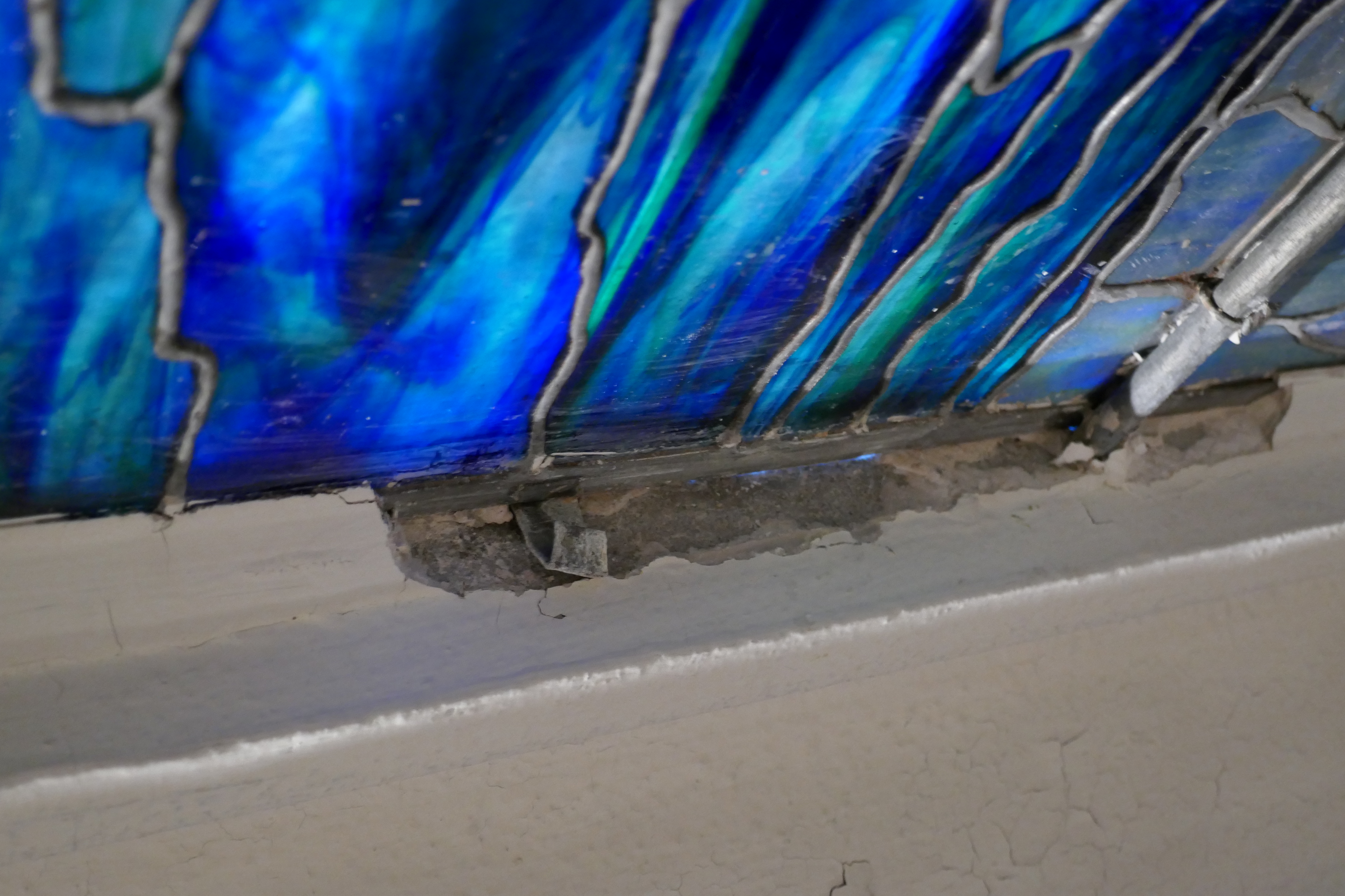 The edge of  blue stained glass next to a damaged section of white wall.