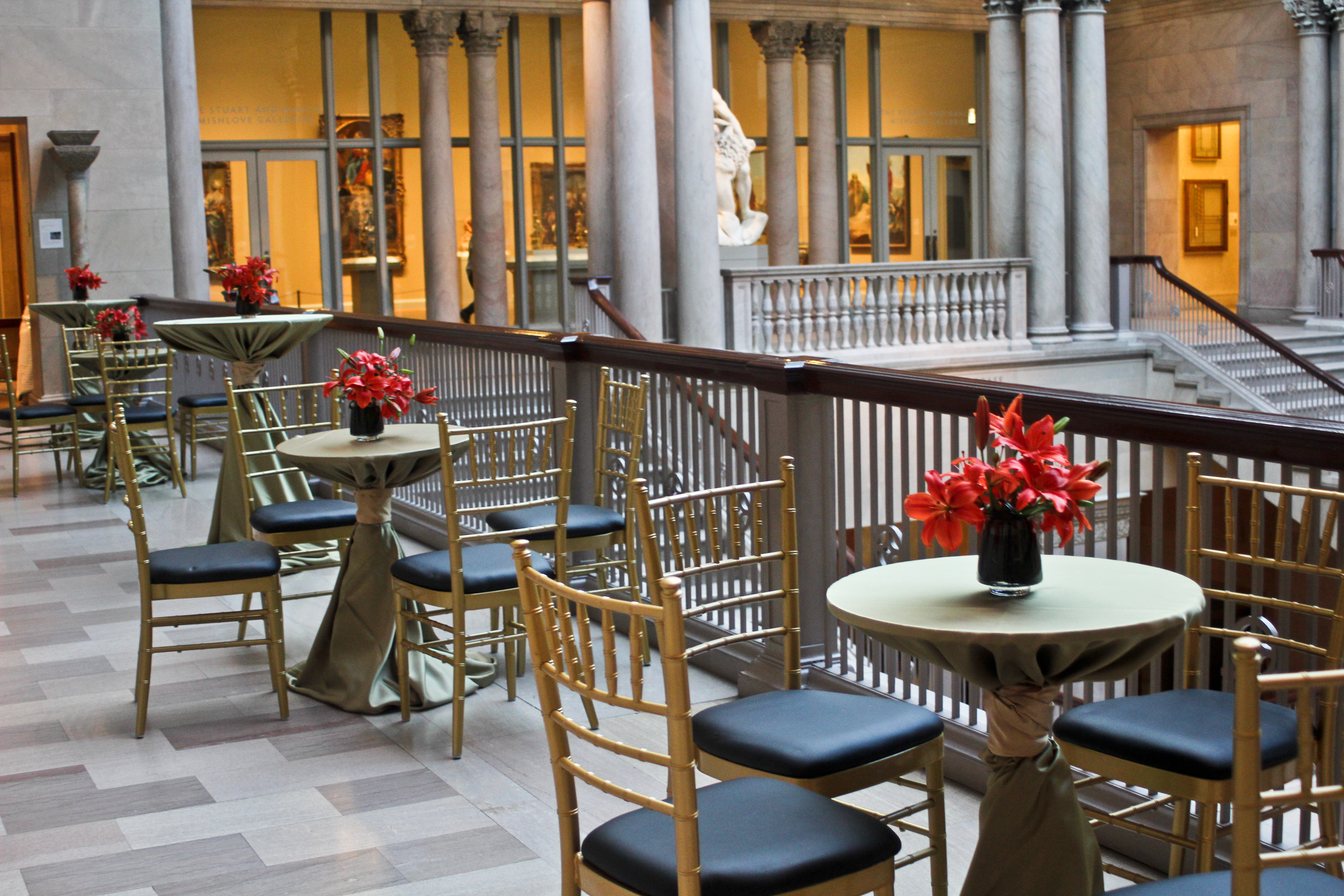 Three gold and black tables sit along side the railing of a grande staircase