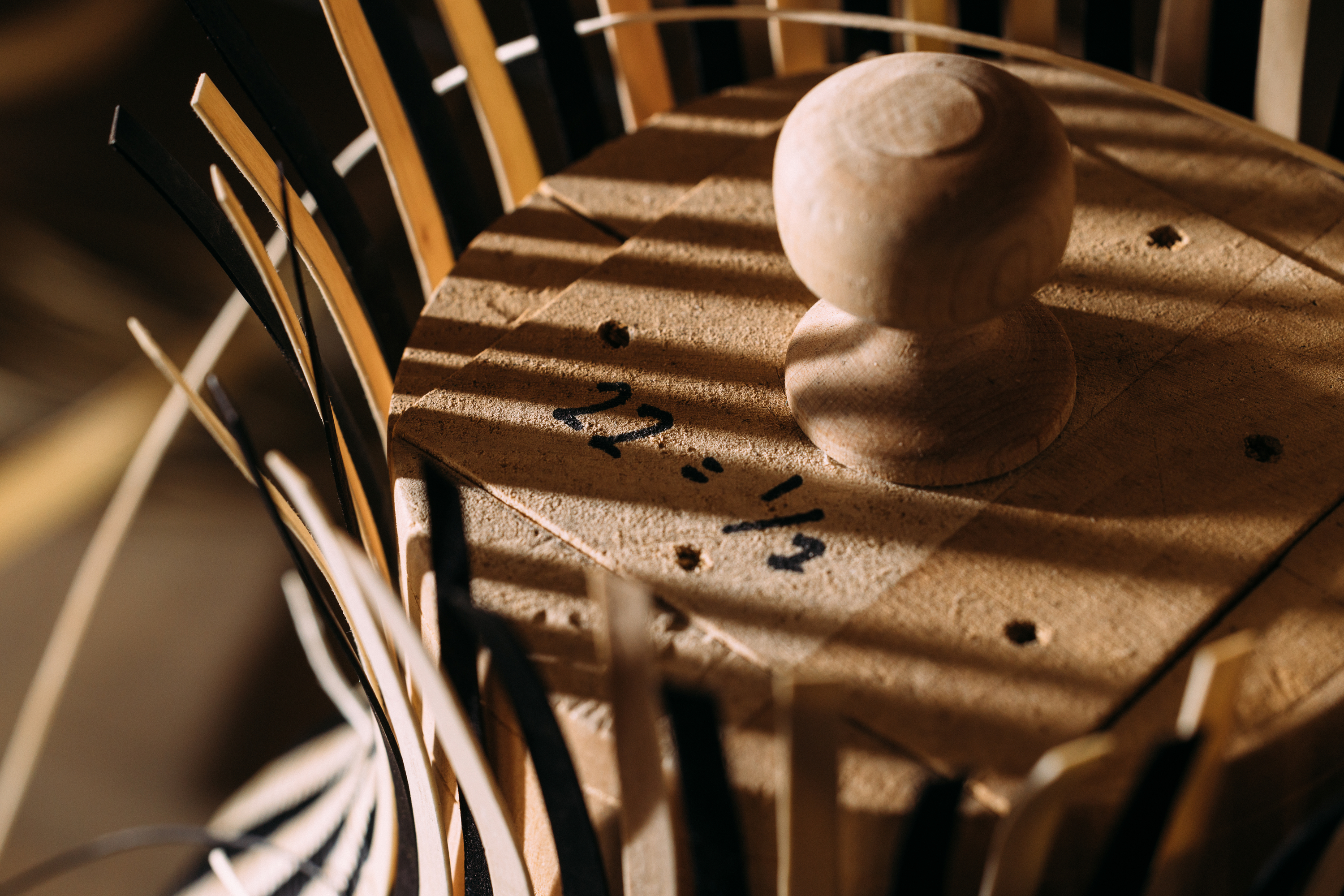 A color photo of the top of a wooden mold with a small knob on top. Thin strips of light-colored wood are placed evenly and vertically around the sides.