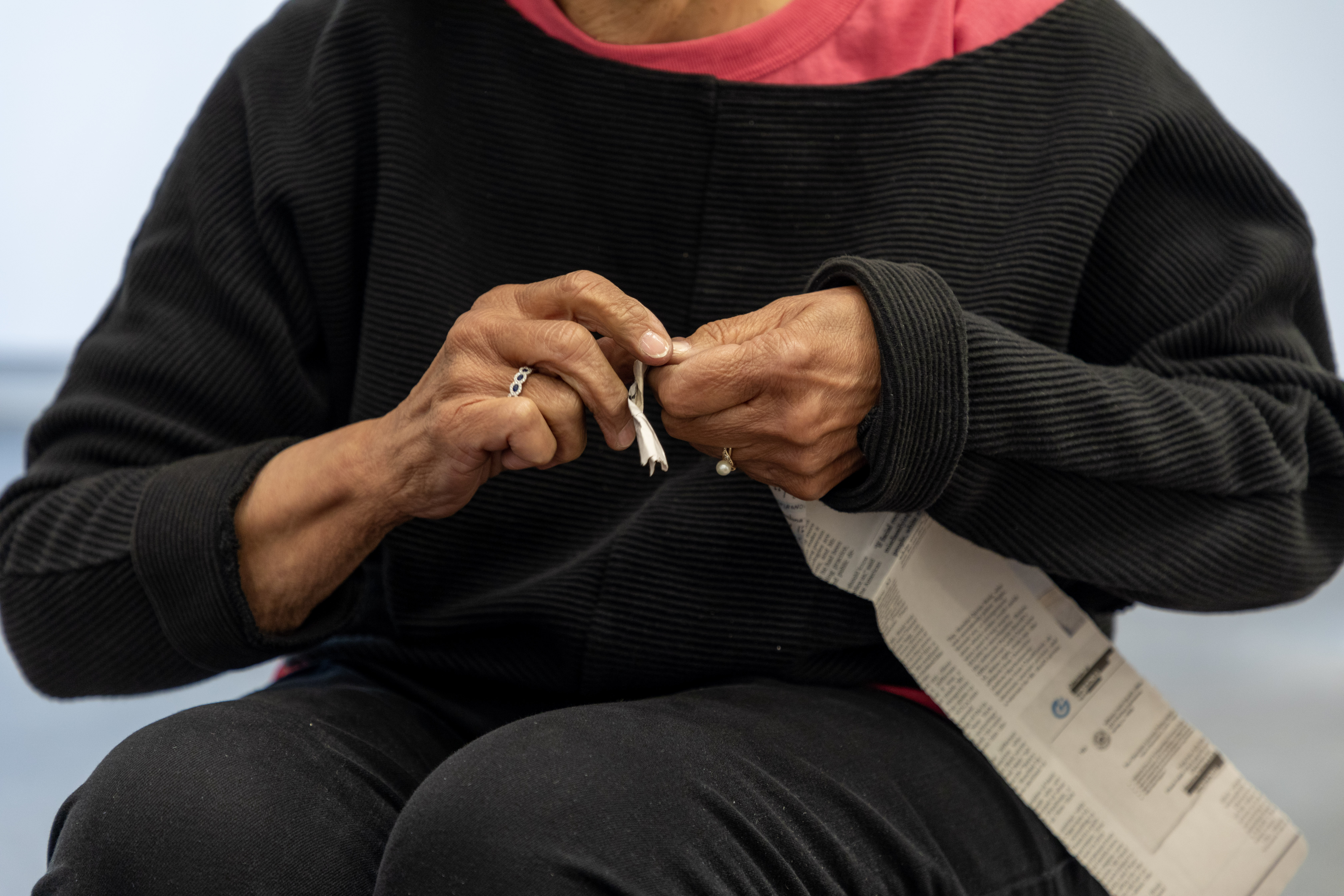Photograph of a dark-skinned woman's hands tying knots out of what seems to be a strip of newspaper.
