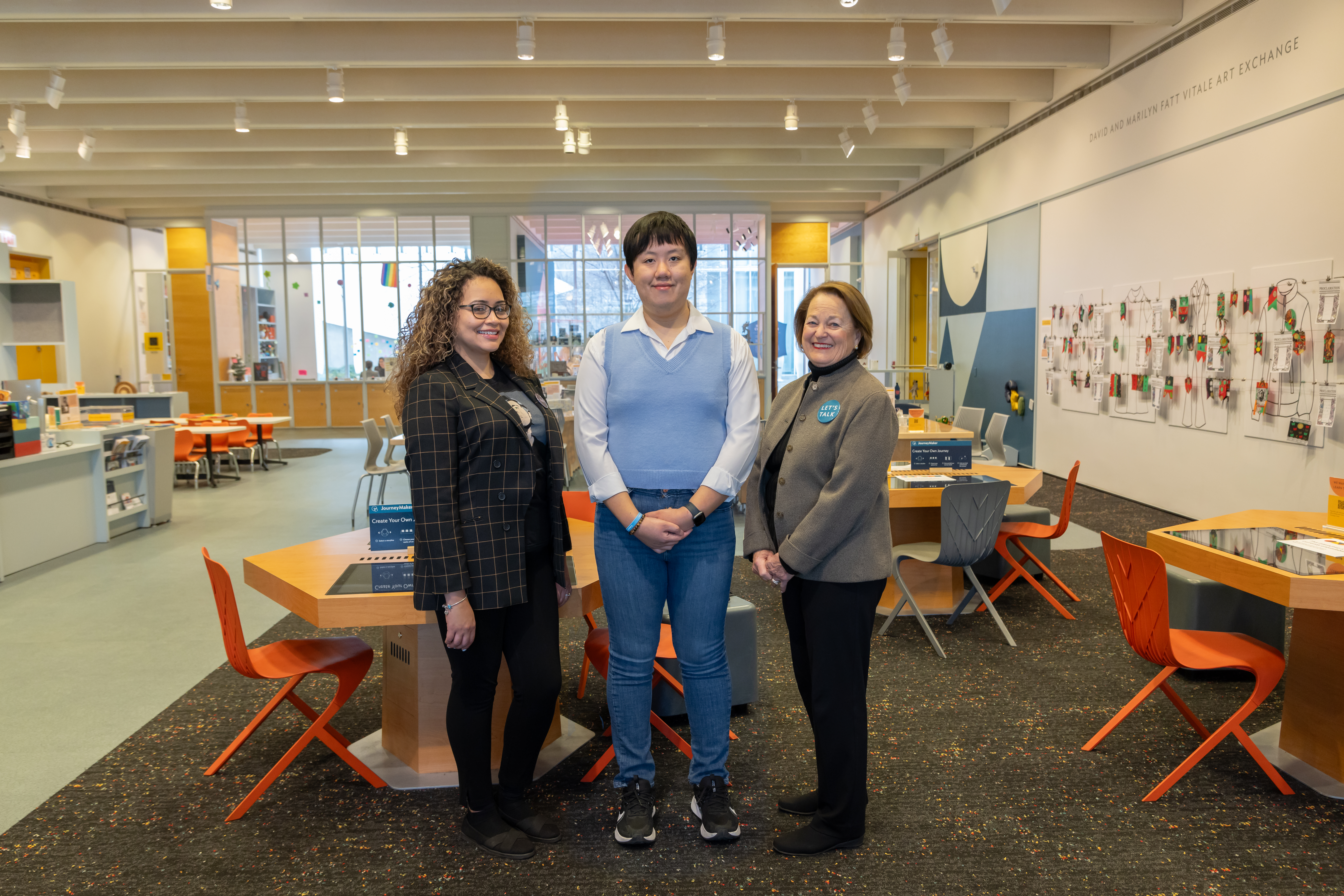 Photo of three adults standing in the Art Institute of Chicago's Ryan Learning Center: at left, Jessica Ramirez, a medium-skinned young woman with long, curly hair dark highlighted in blond, wearing a dark jacket; in the middle, Hugo Nugraha, a young light-skinned man with dark hair, wearing a light-blue vest; and at right, Kathy Sargent, an older woman with light skin and medium-brown hair, wearing a brown jacket.