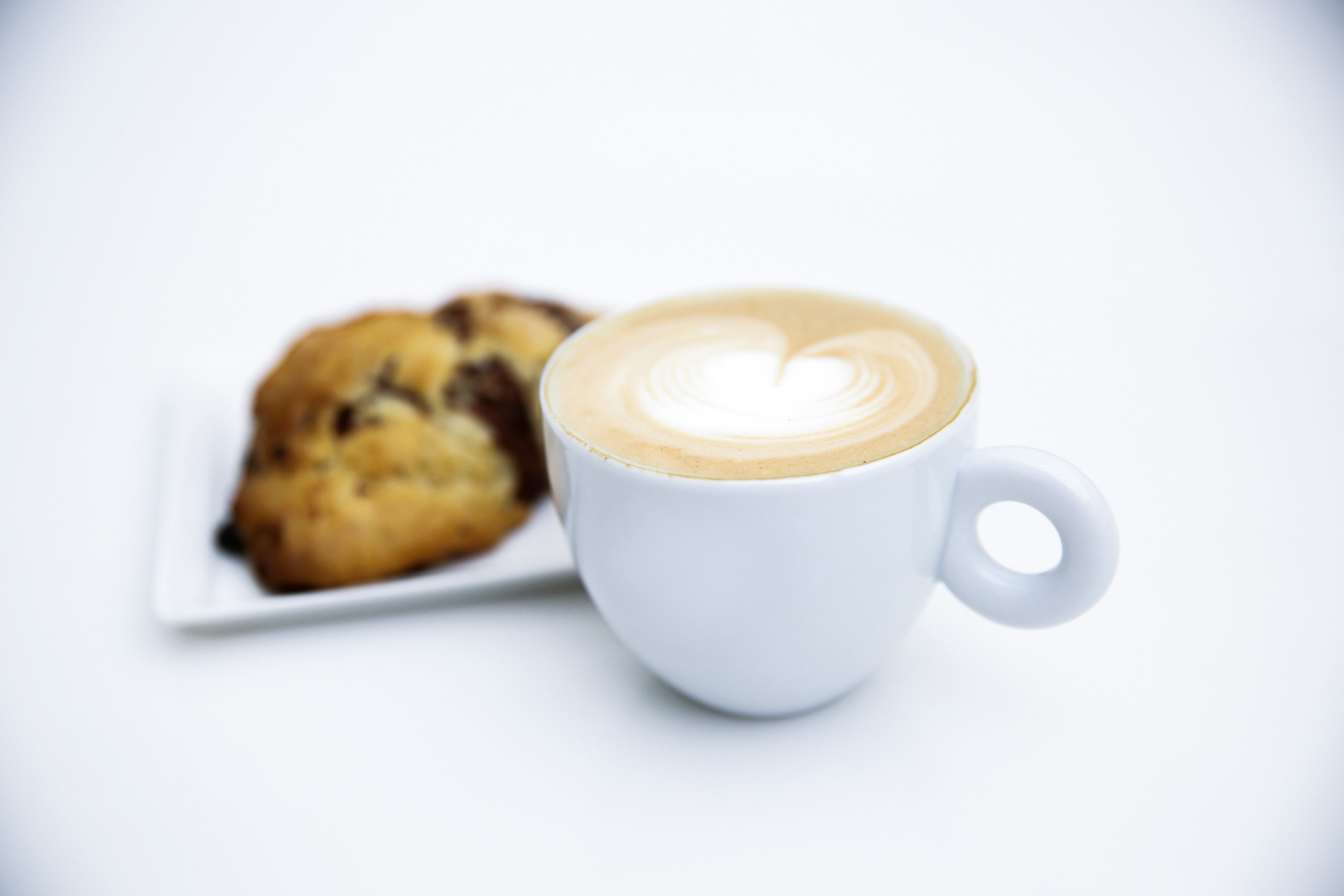 A coffee drink and a scone on a white plate.