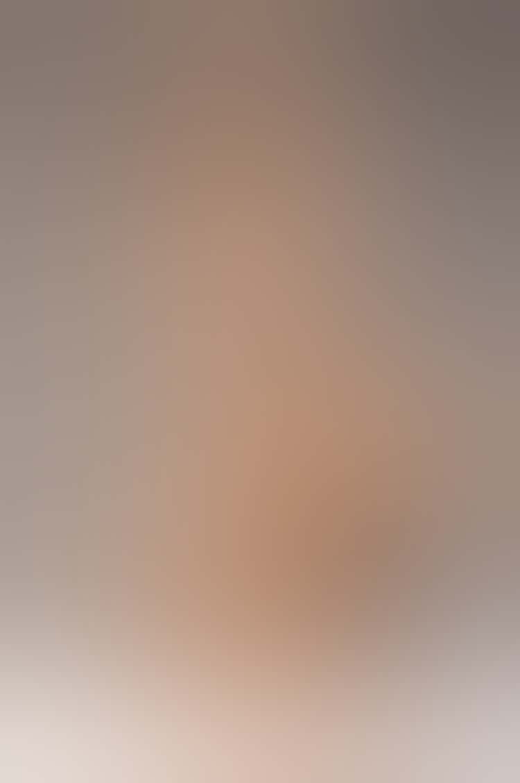 A light-toned sculpture of a nude young woman. She sits on an ambiguous grooved support, looking slightly down to the right. Her right arm bends to touch her fingers to her right shoulder, and her knees point inward as her feet separate on the support. Behind her is an undefined modeled form.