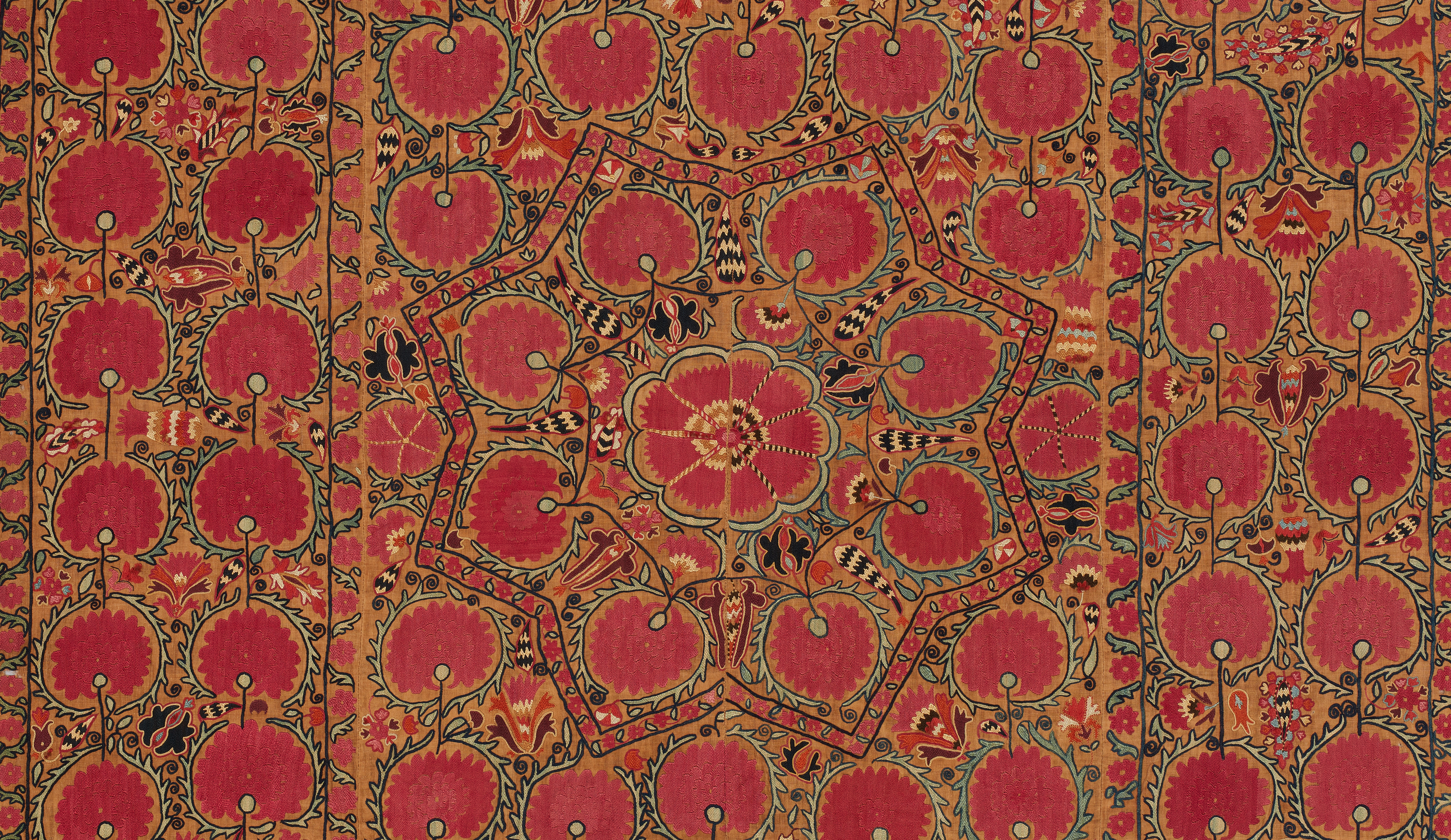 A photograph of a patterned textile shows a red flower at center within a star-like frame on a gold background with black and green outlines; rows of red circular motifs with small pale dots fill the field, with matching vertical bands at left and right.