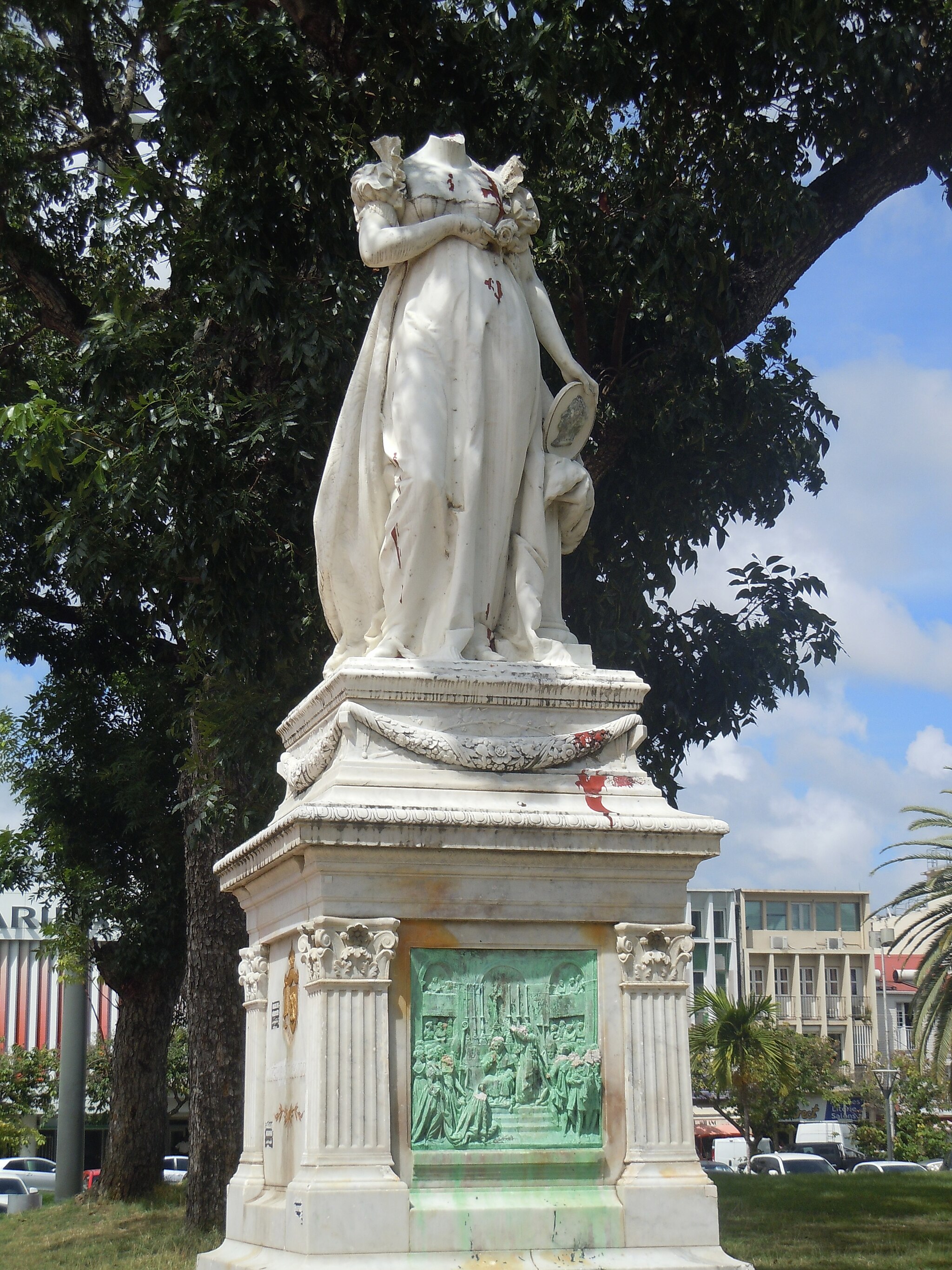 Photo shows a white marble sculpture of a female figure in a short-sleeve gown whose head has been removed.
