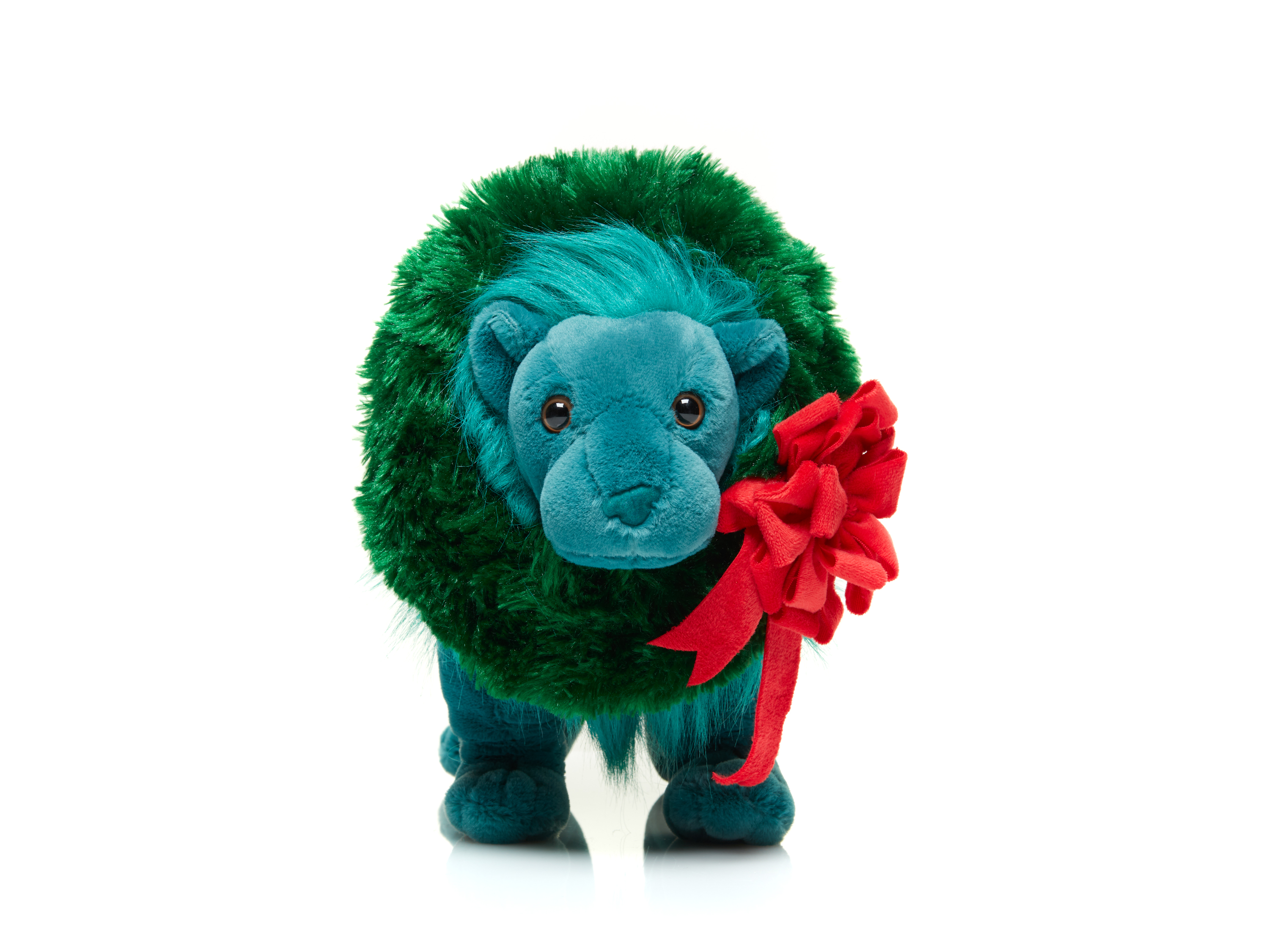 A teal-green plush lion wearing a green plush wreath with a large red bow faces the viewer head-on.