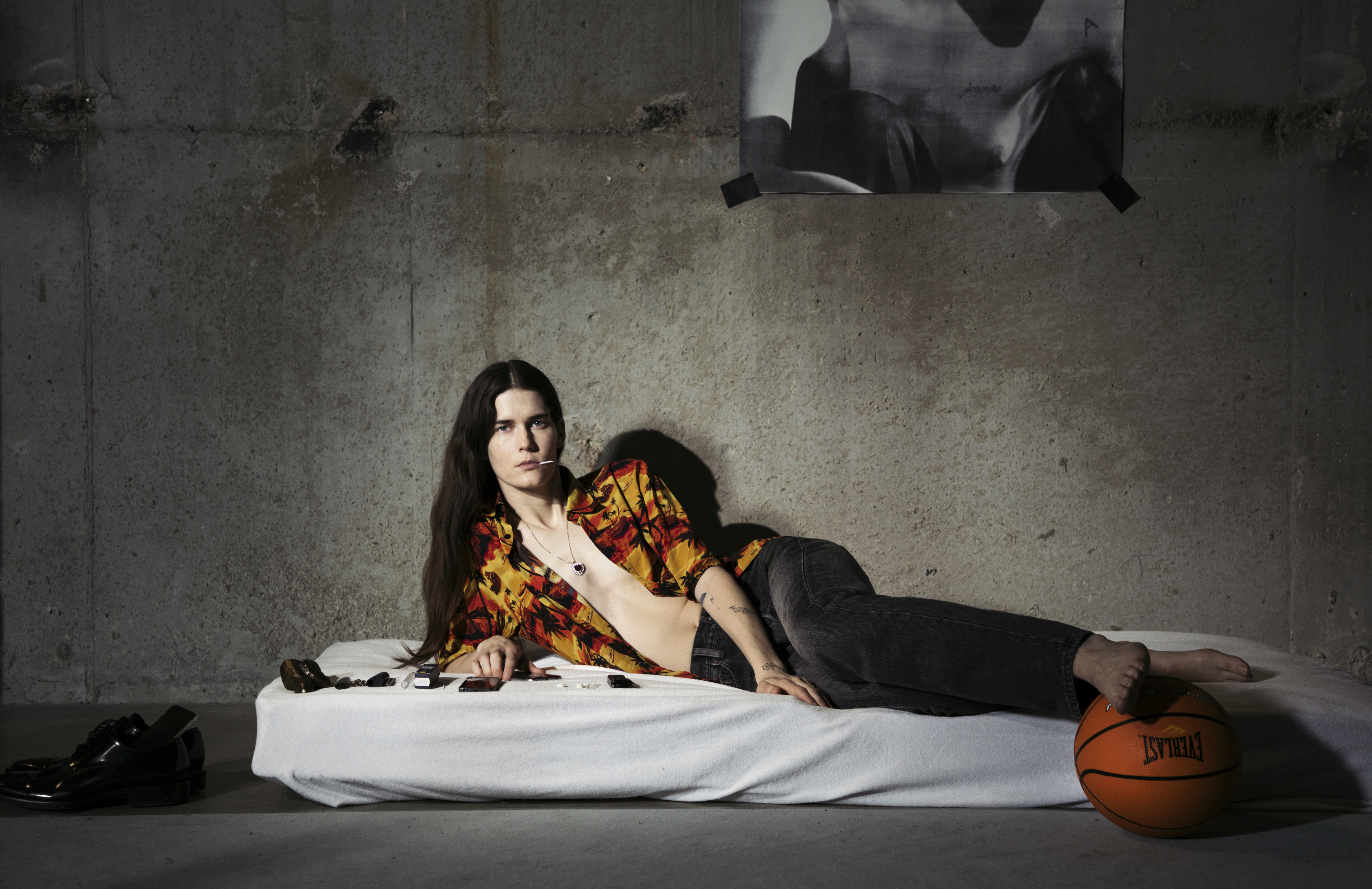 A photograph of a woman lying on her side on a mattress in a concrete room.