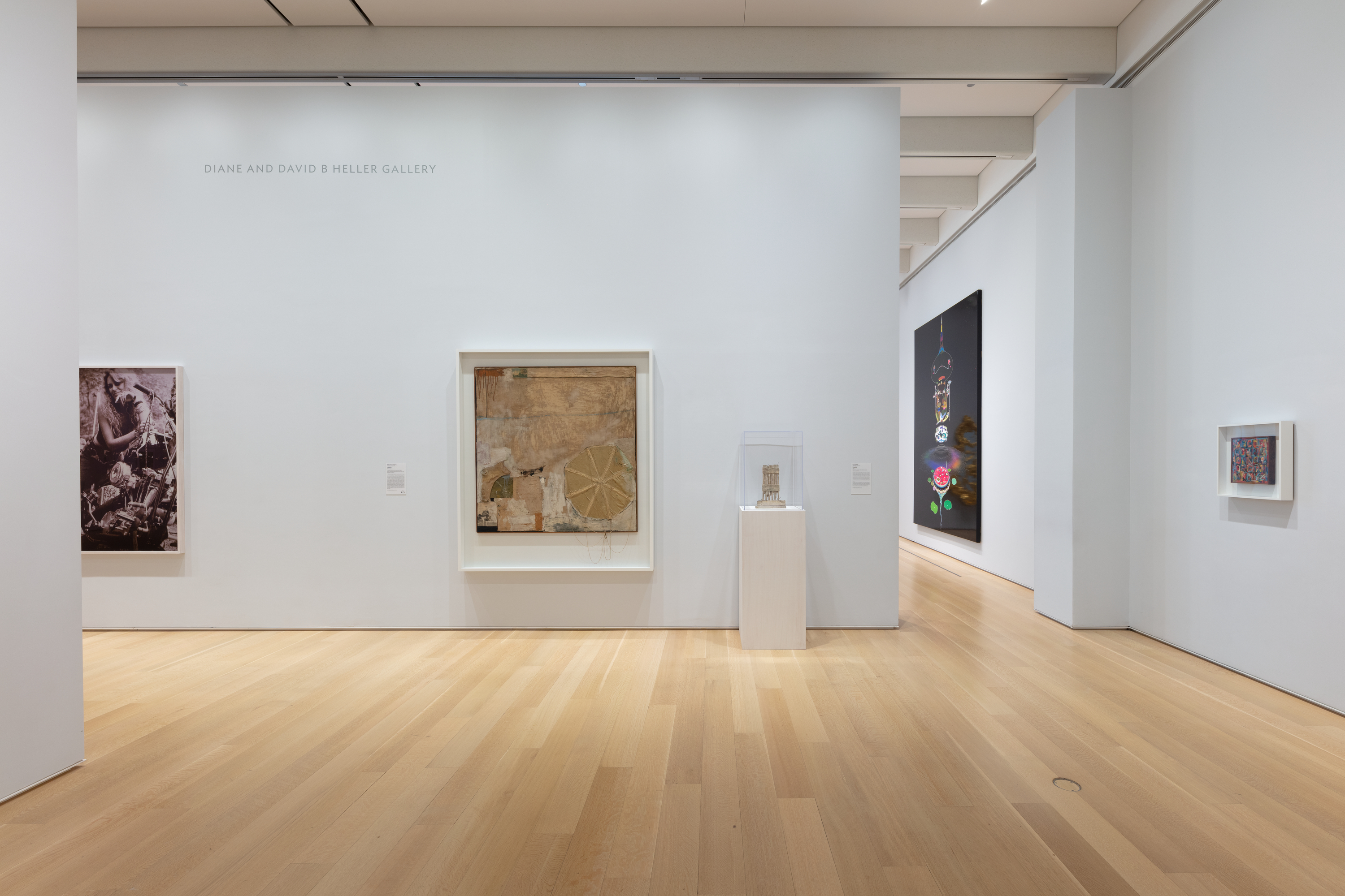 Photo shows the corner of a white-walled art gallery featuring numerous works of contemporary art, including Robert Rauschenberg's "Untitled, 1955" at center.