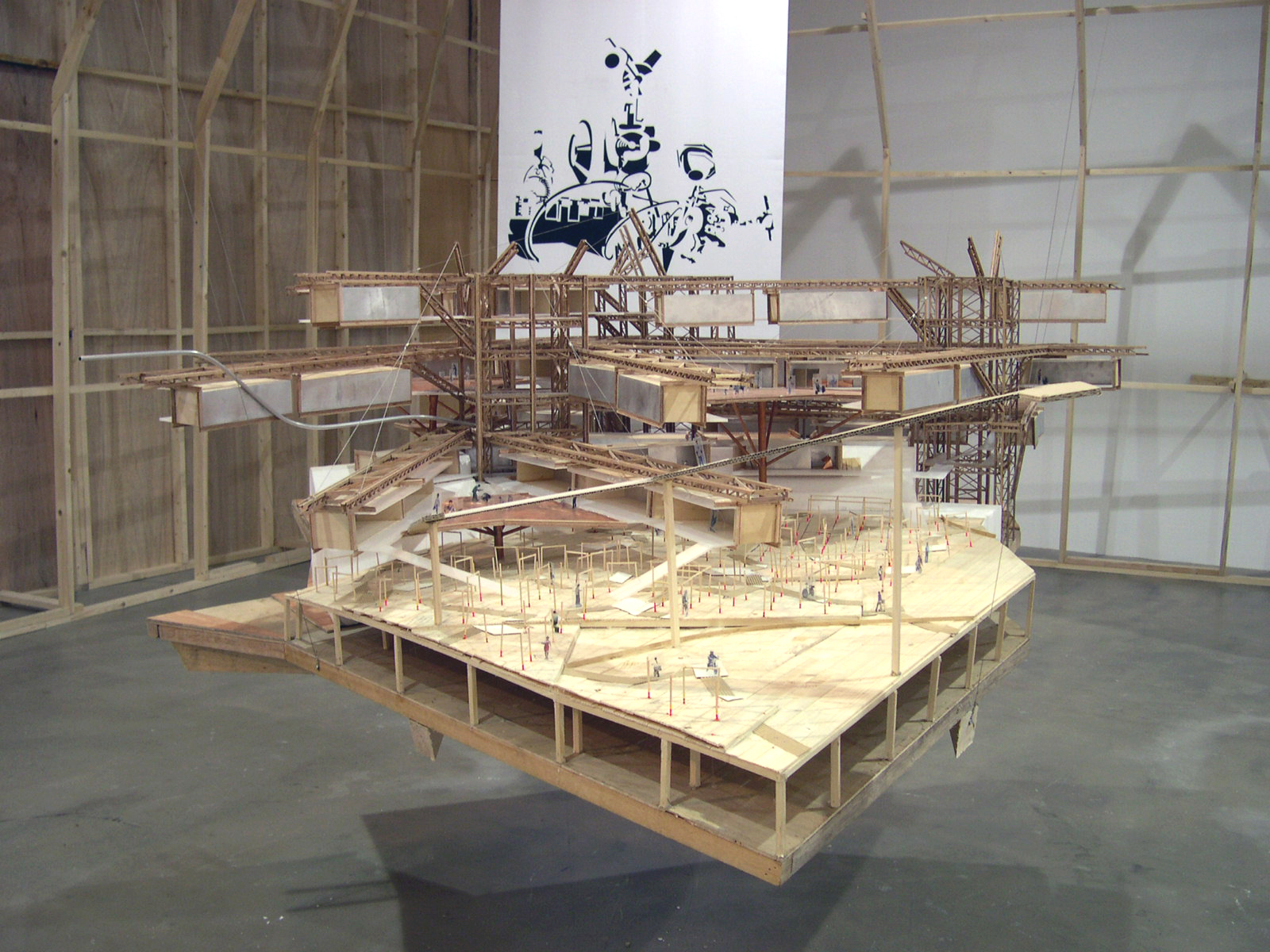 A model made of cardboard, tape, and strings prominently featuring a cardboard ramp held up by thin wooden supports. Beams made of cardboard and string are suspended below small structures made of wood. The structure rests on a wooden platform.