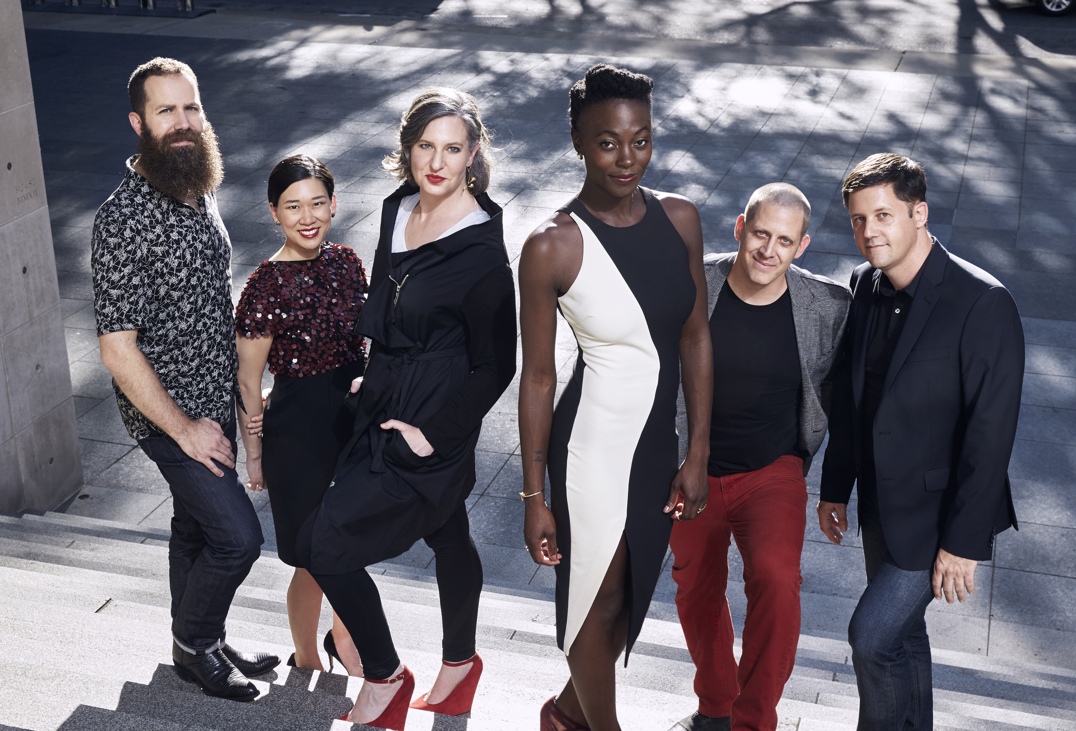 A color photograph of a group of three men and three women posing as a group and looking at the photographer.