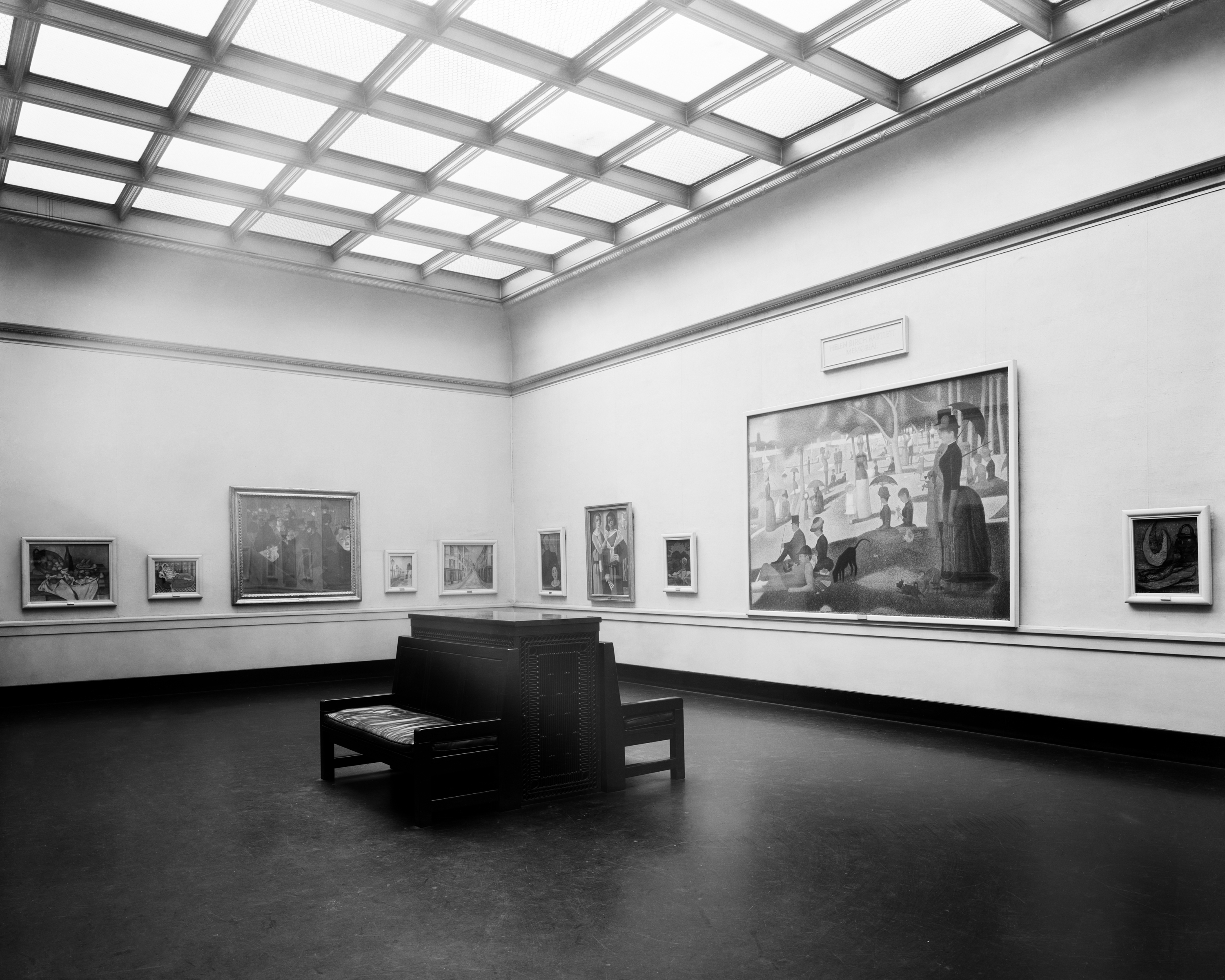Black-and-white photograph taken at an angle of a wide gallery space featuring Seurat's "La Grande Jatte" in a slim white frame.