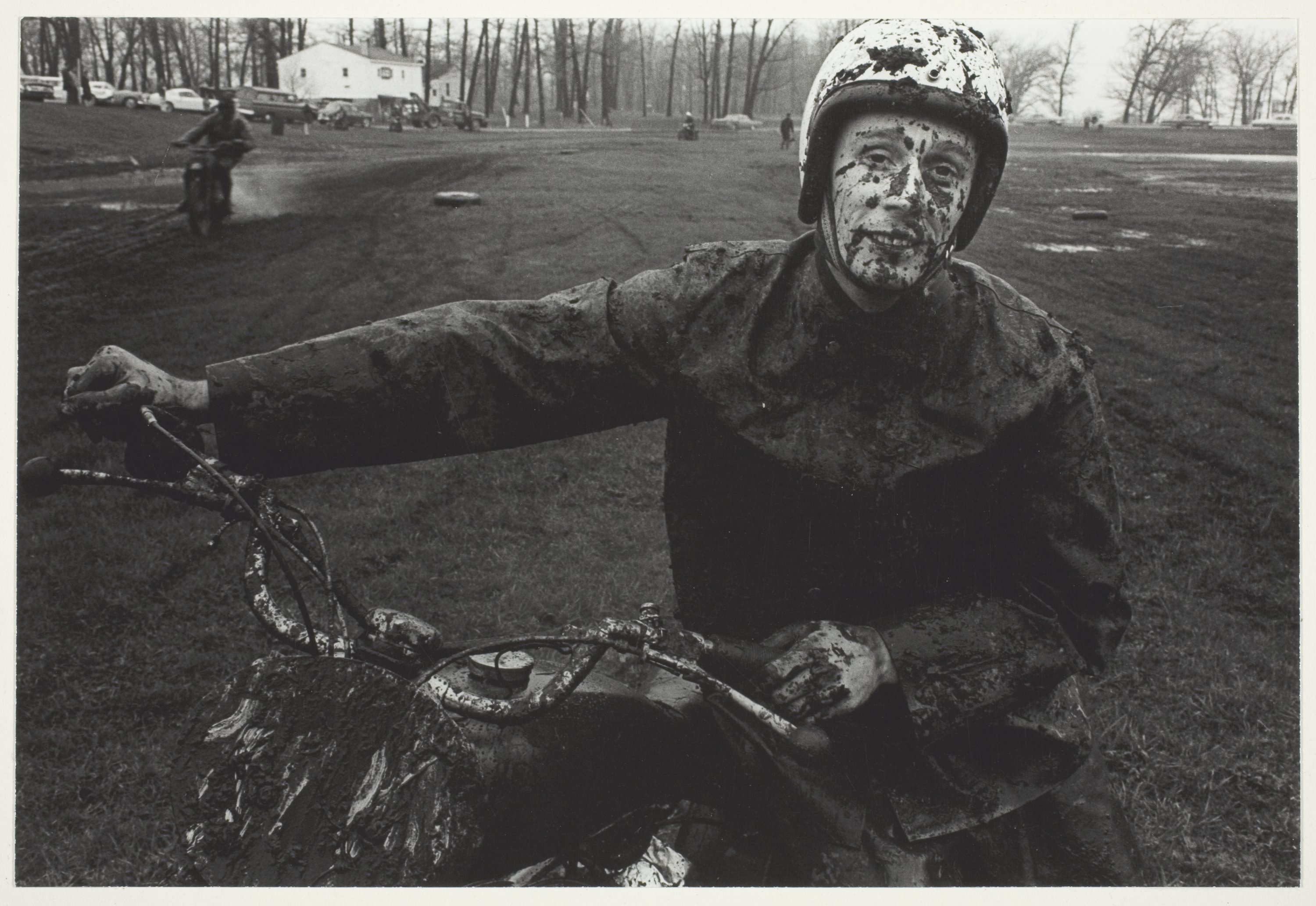 A photo of a man on a motorcycle with his face, hands, and clothes spattered with mud.