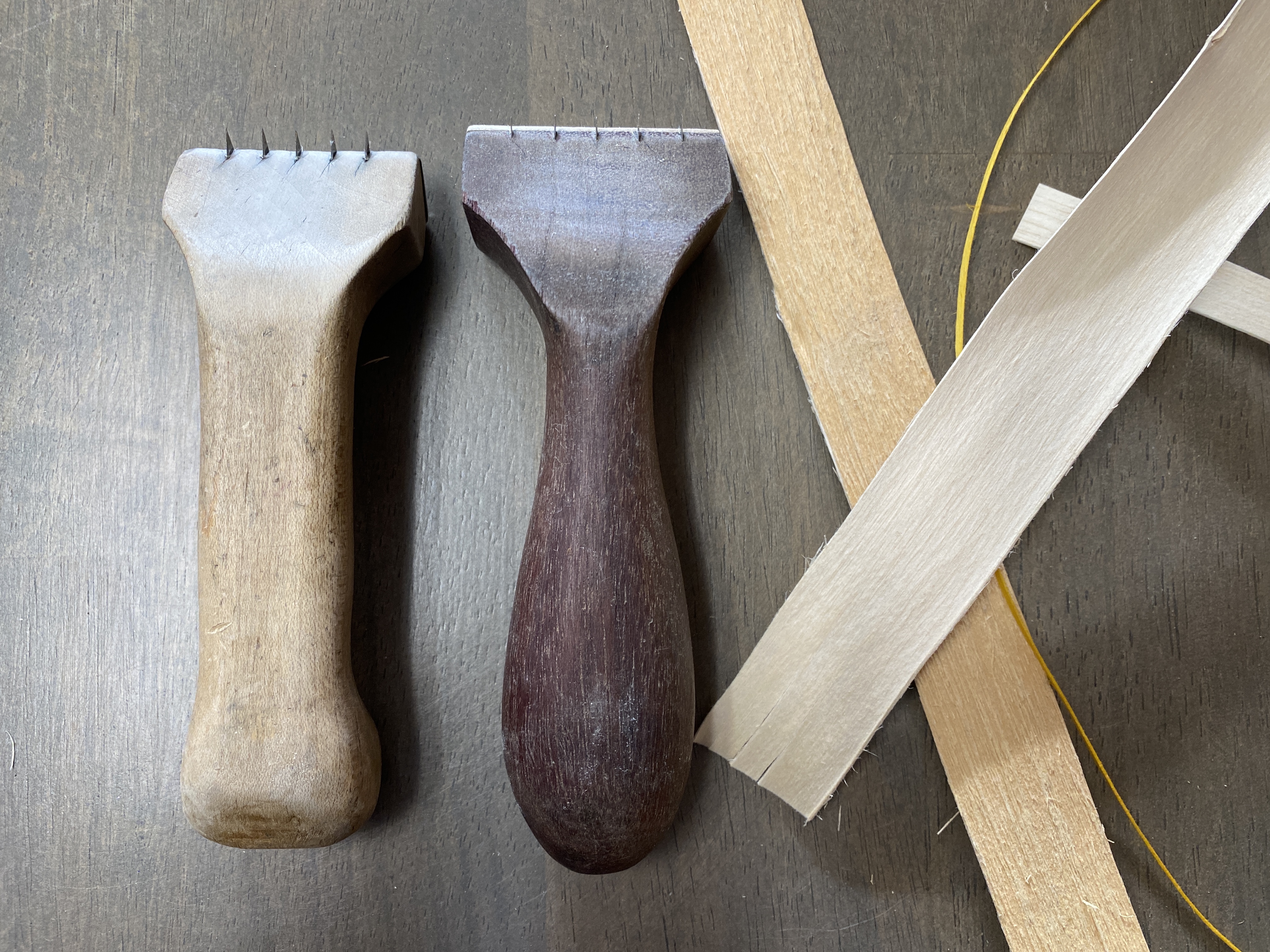 A color photo of two wooden tools, one a lighter wood and one darker, consisting of a handle and a wider end with several small metal blades.