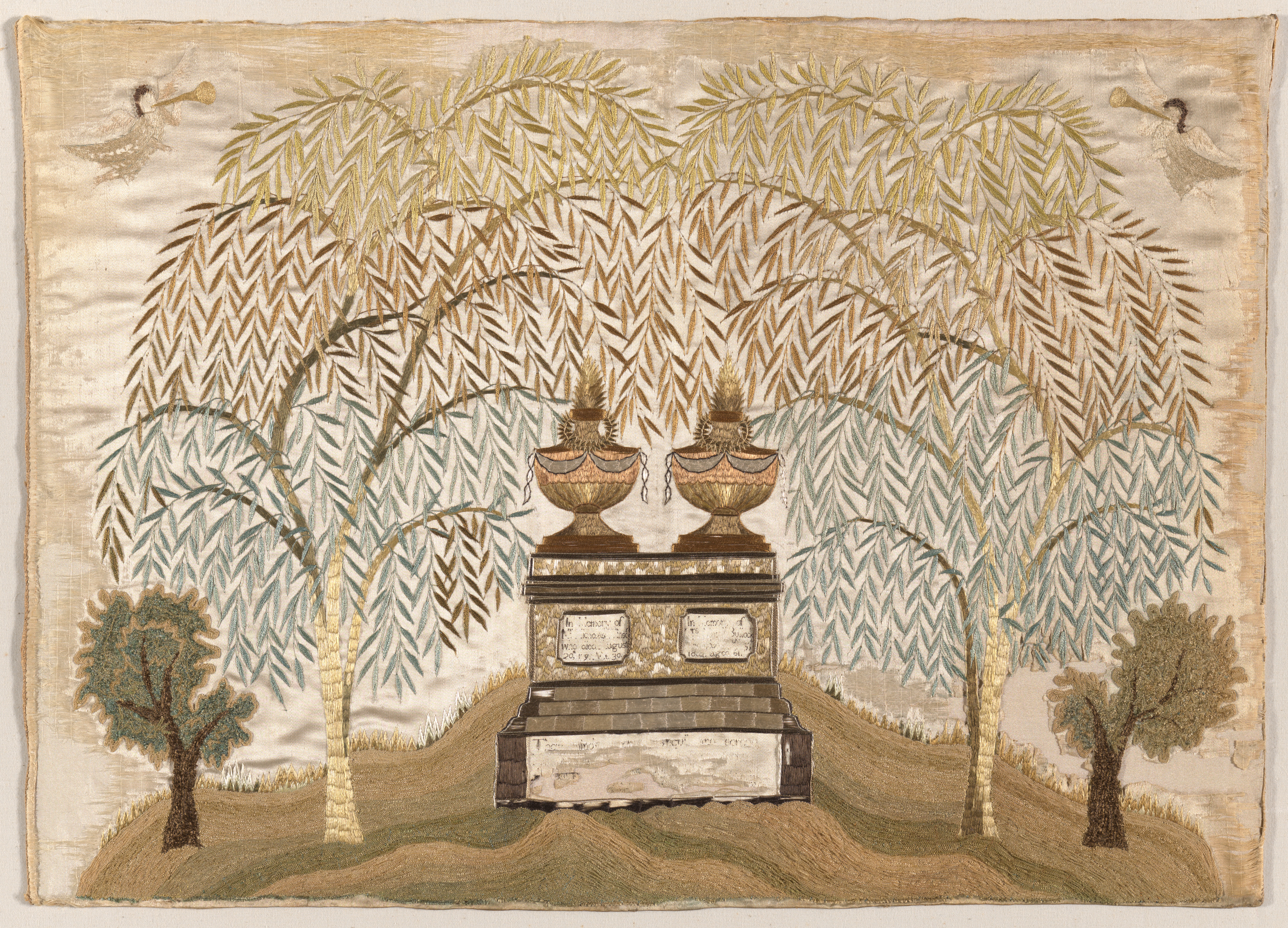 An embroidered textile in shiny green and brown thread shows a gravesite with a rectangular stone topped with two unlike structures. Two plaques on the stone are embroidered with text, much of it missing. Willow trees and their leaves fill the background.