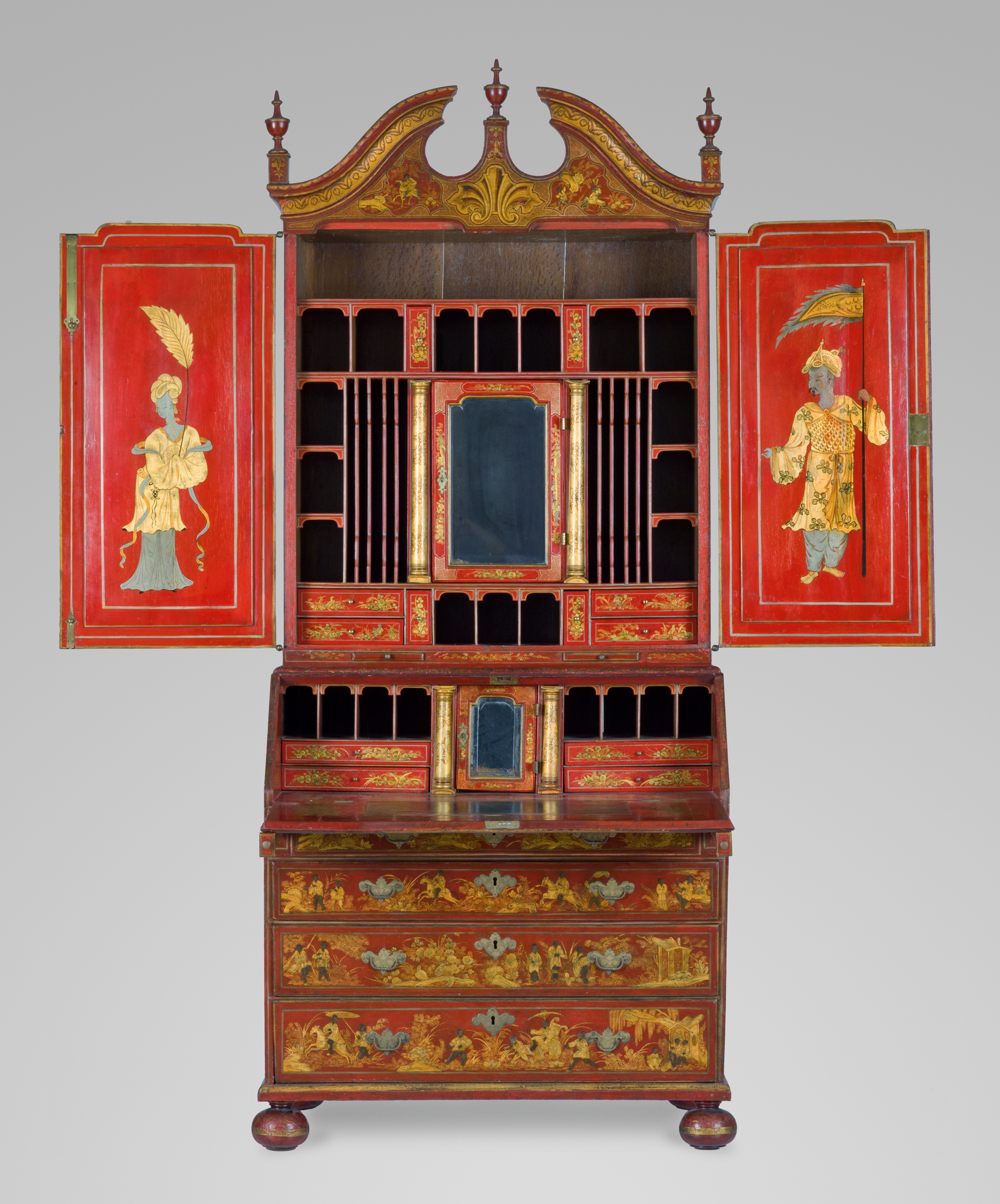 A lacquered red cabinet decorated with a broken pediment. On the interior doors, a lady holding a branch faces a warrior holding a banner. The slope front is richly decorated with figures riding in a chariot, while others lounge in summer pavilions. The drawers and slides display landscapes with horsemen and other figures, birds, and foliage.