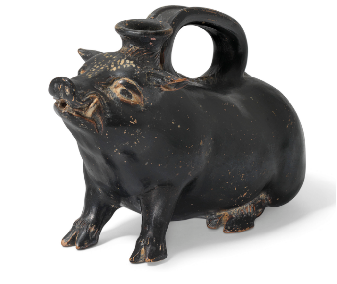 A boar-shaped vessel, dark colored, with a handle at top and a spout between the ears.