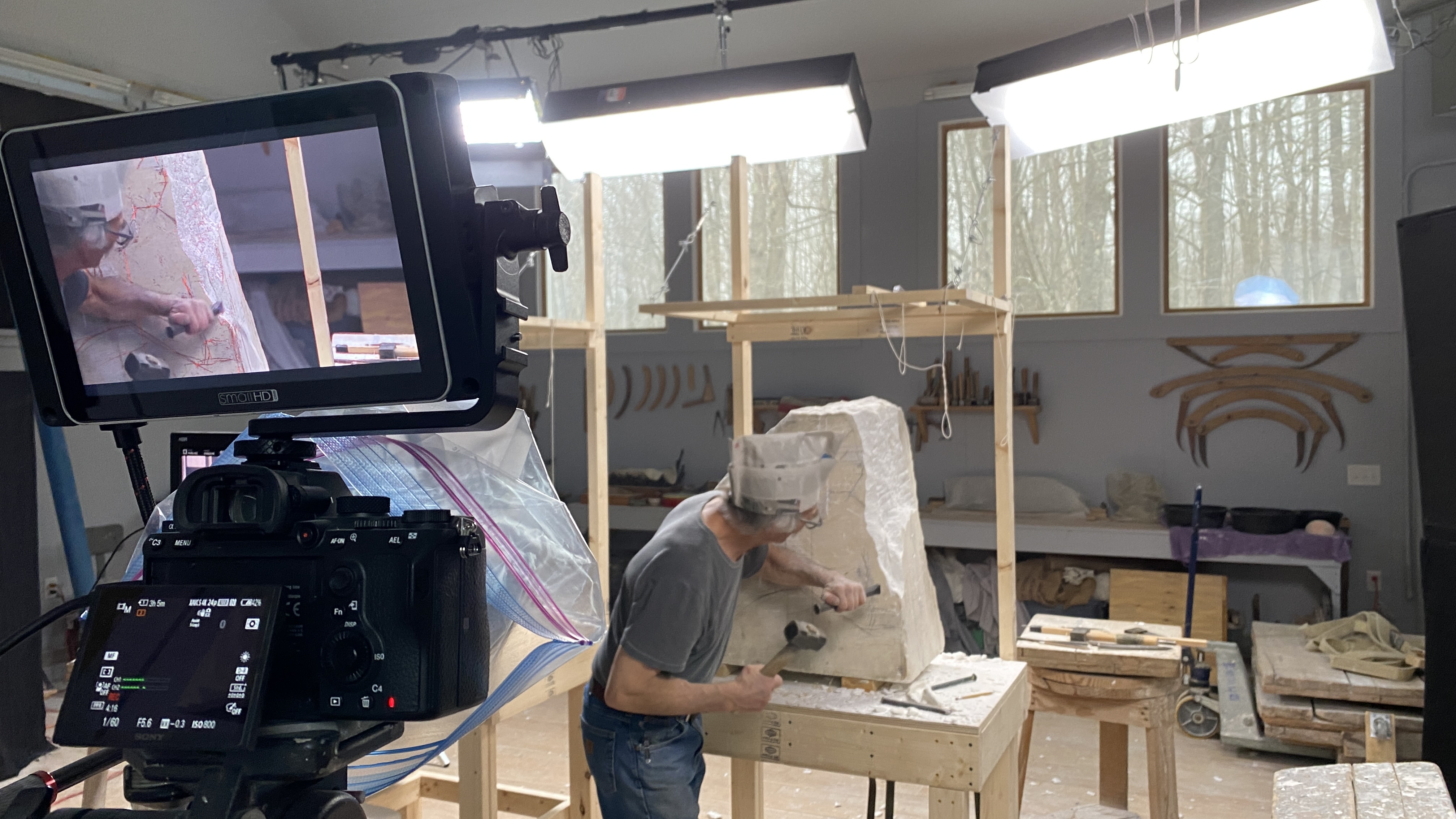 Color photograph of a older man chipping away at a piece of marble with a chisel in one hand and a hammer in the other.