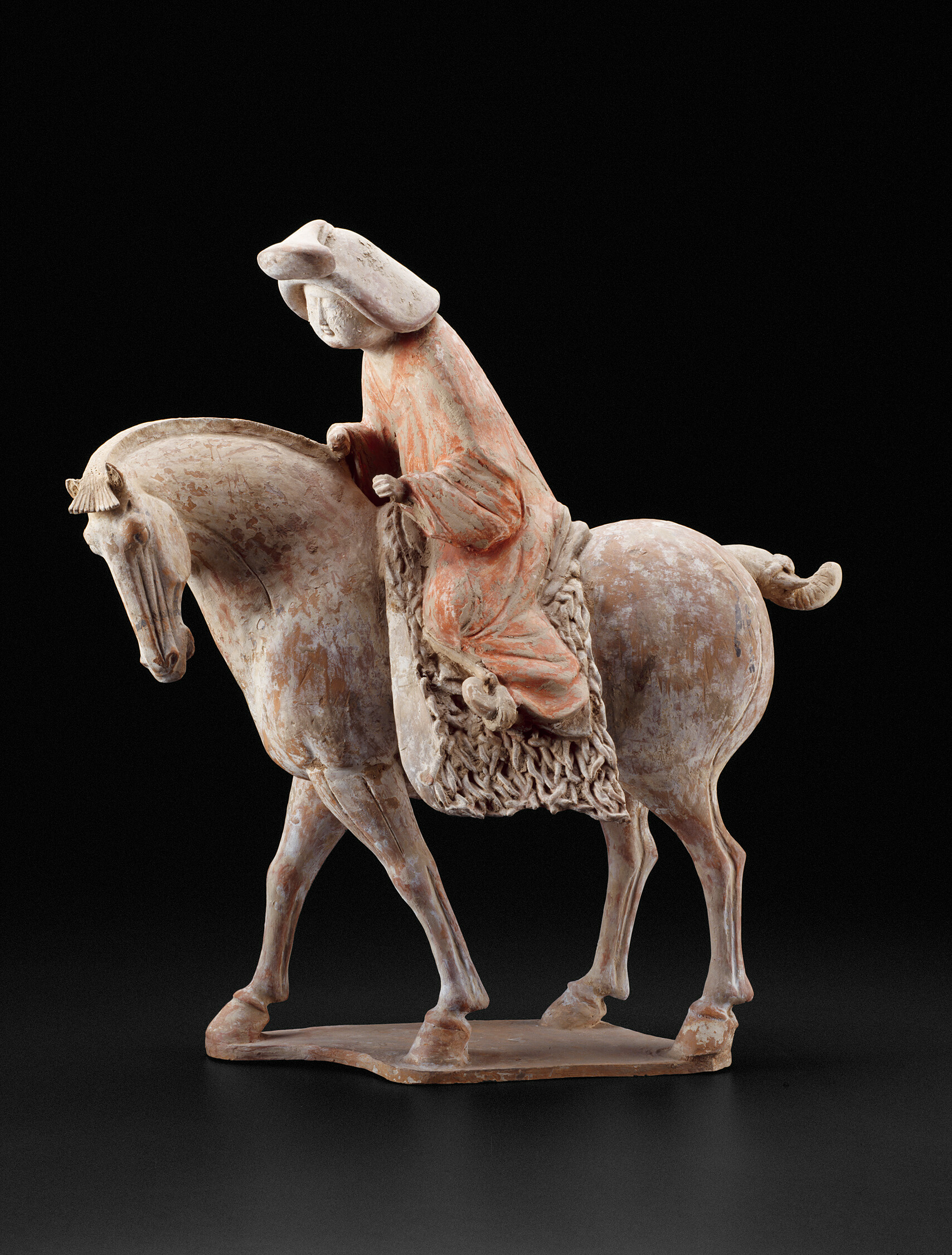 Ceramic sculpture of a figure in a red robe and white head covering atop a horse.