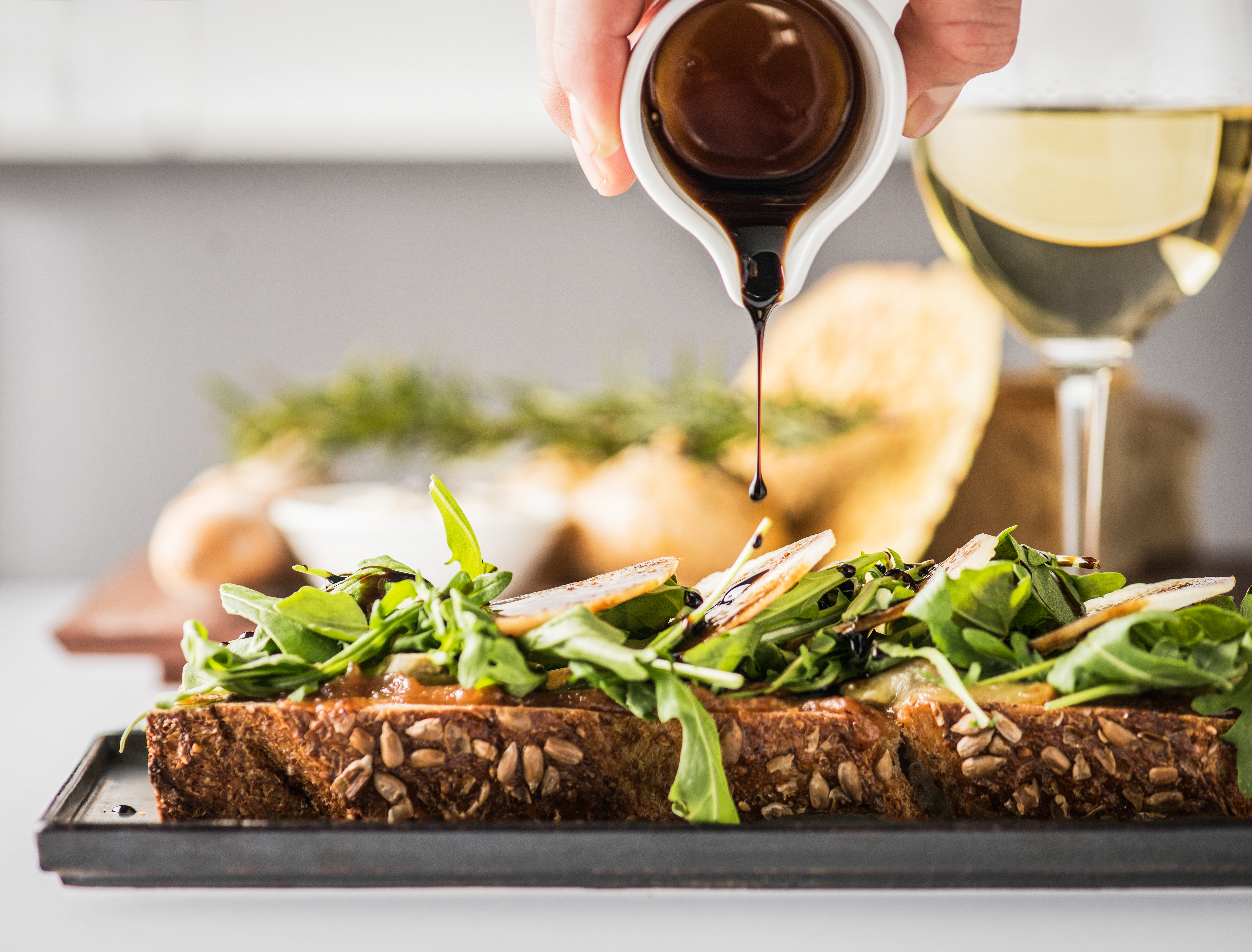 A hand pours sauce onto a open face sandwich