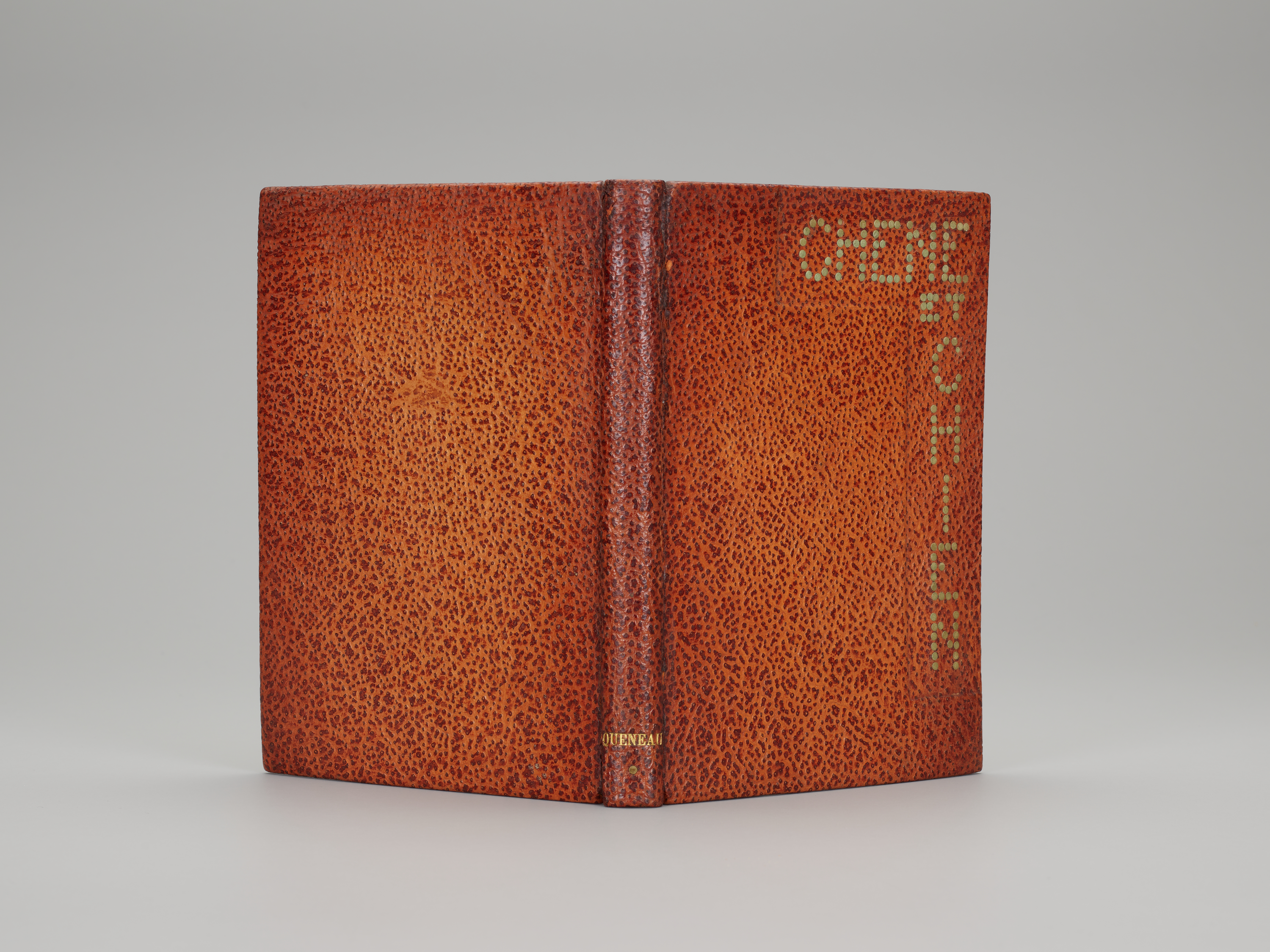 A book binding in orange-brown pebbled letter with the words "CHENE ET CHIEN" running along the top of the front cover and down the right side. The font is composed of small beige circles. The book is positioned upright and open, its spine facing the viewer.
