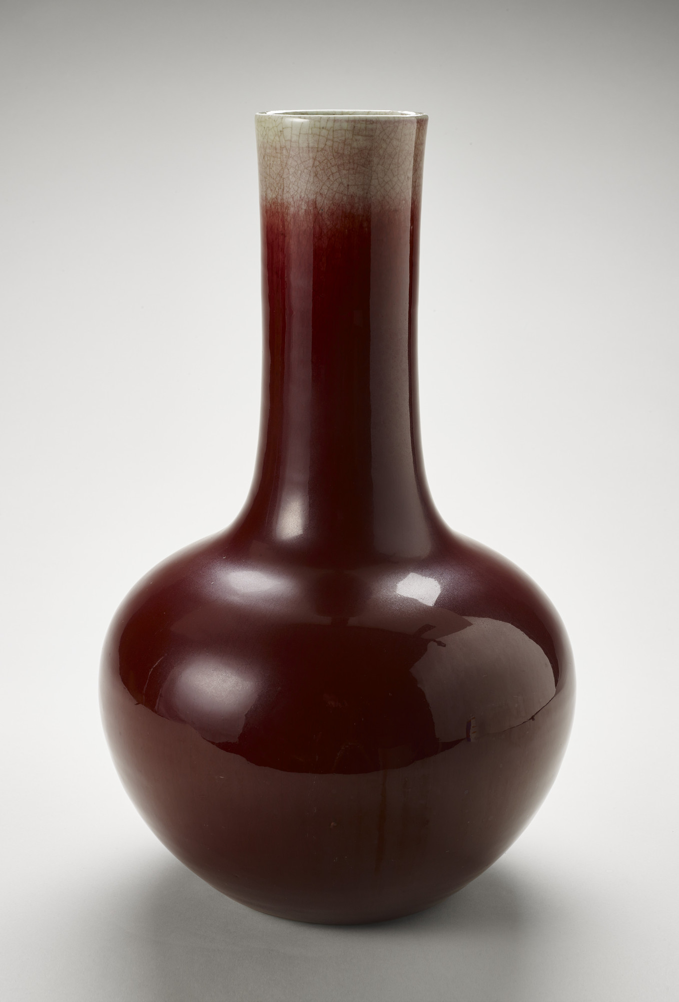 A very deep red, almost brown, ceramic vase with a bulbous base and a long, thin neck with a cream-colored upper region.