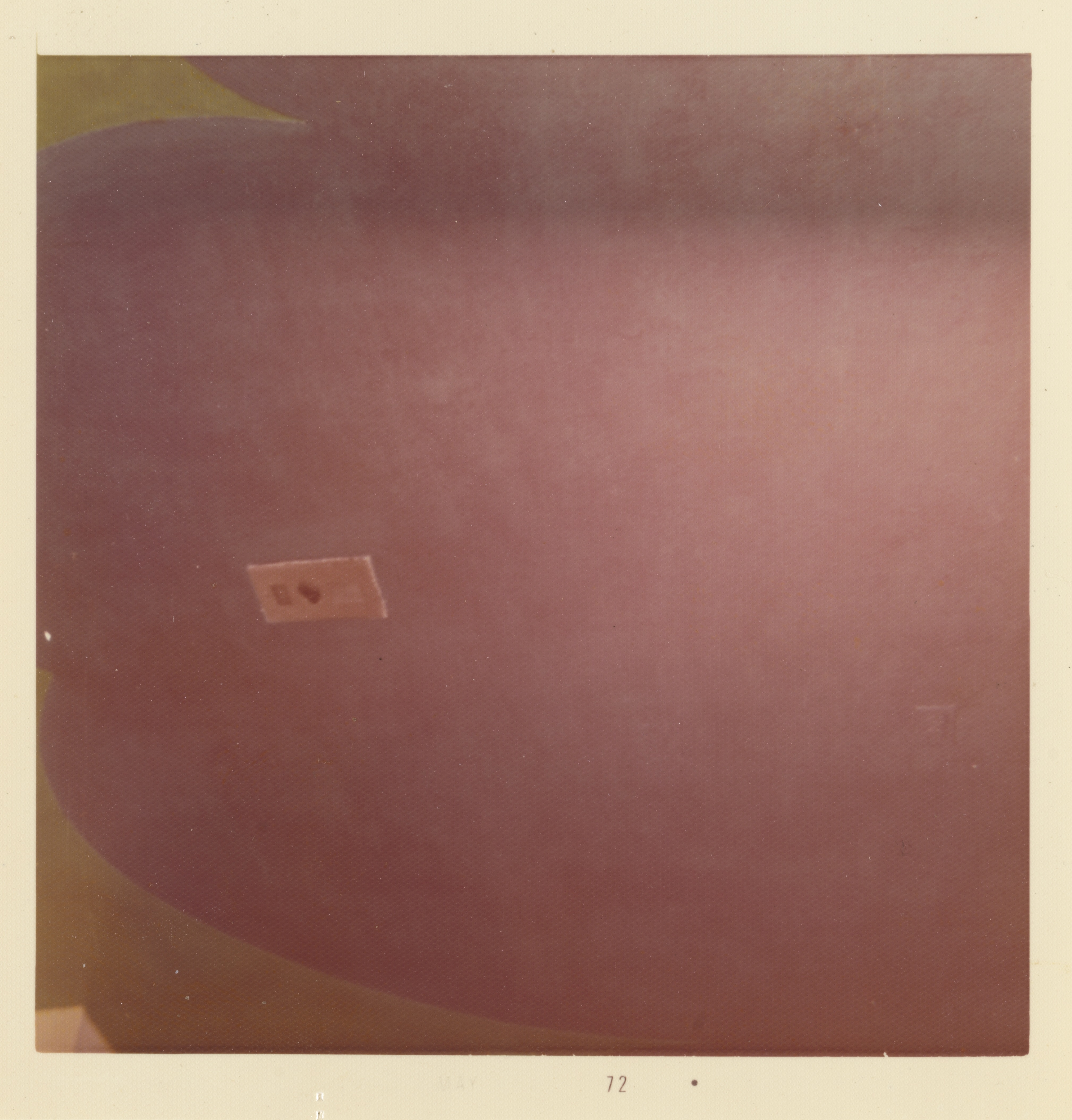 Photograph of a curved mauve-painted wall with a smooth gradient of darker tones toward the top. Near the center, a small rectangular label is affixed to the wall, showing the number “13” next to a heart symbol. The bottom left corner shows a glimpse of a yellow shape overlapping the mauve background. The white border of the print includes the number “72” centered along the bottom edge.