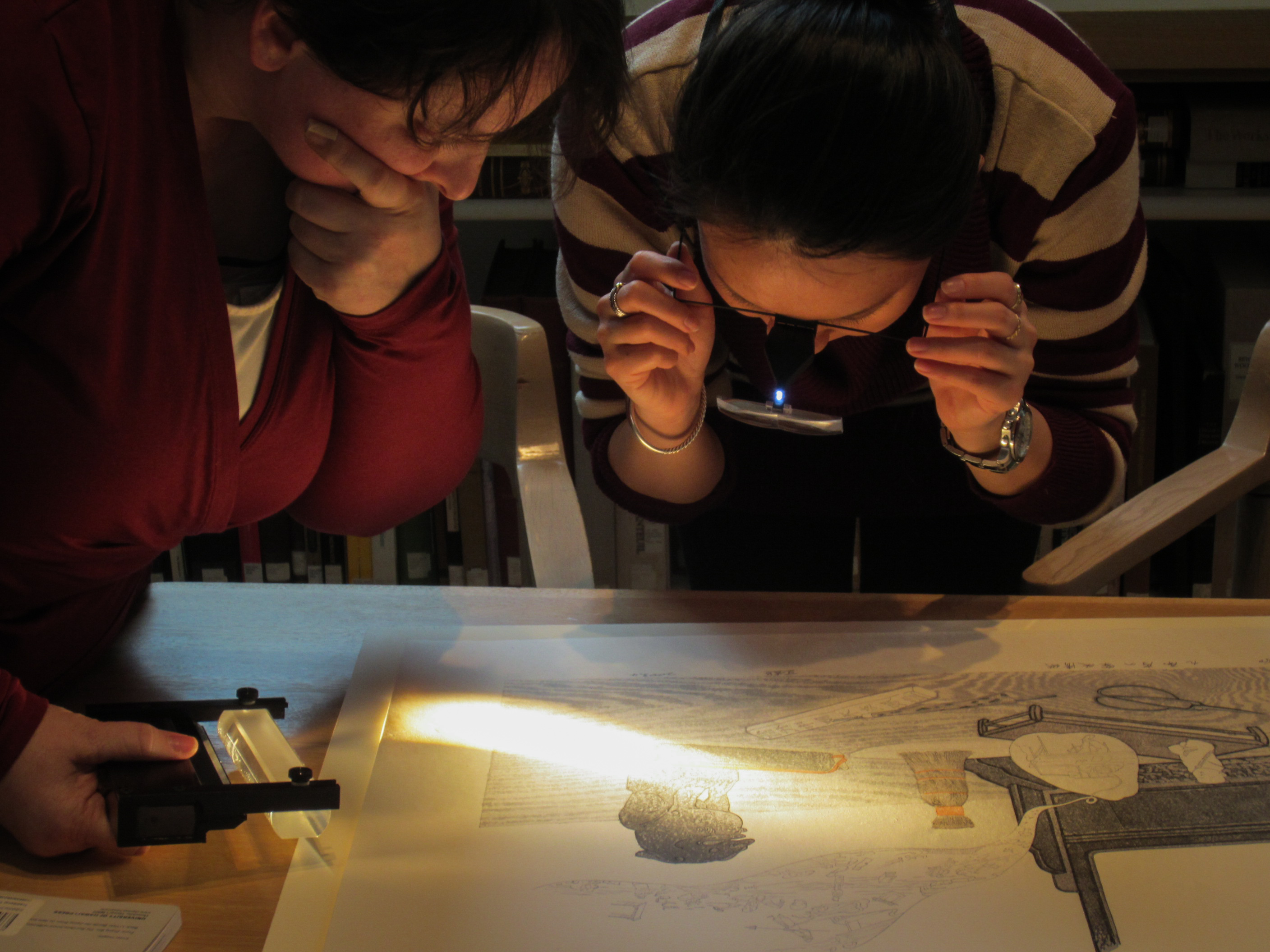 Two people look at an artwork under a magnifying glass