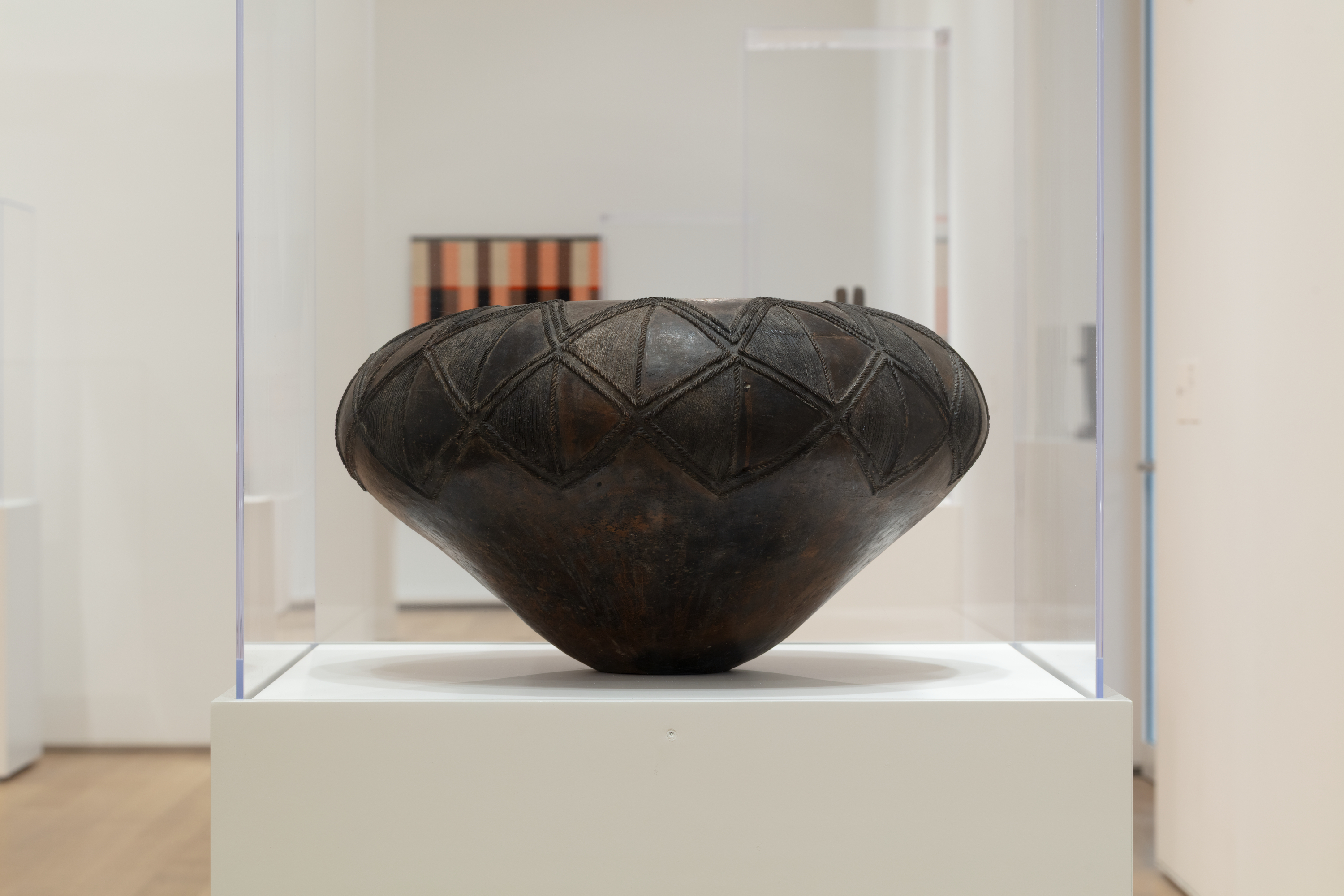 A ceramic vessel with a wide, rounded top that narrows to a slim base. It is decorated with a pattern of repeating diamond shapes in relief.