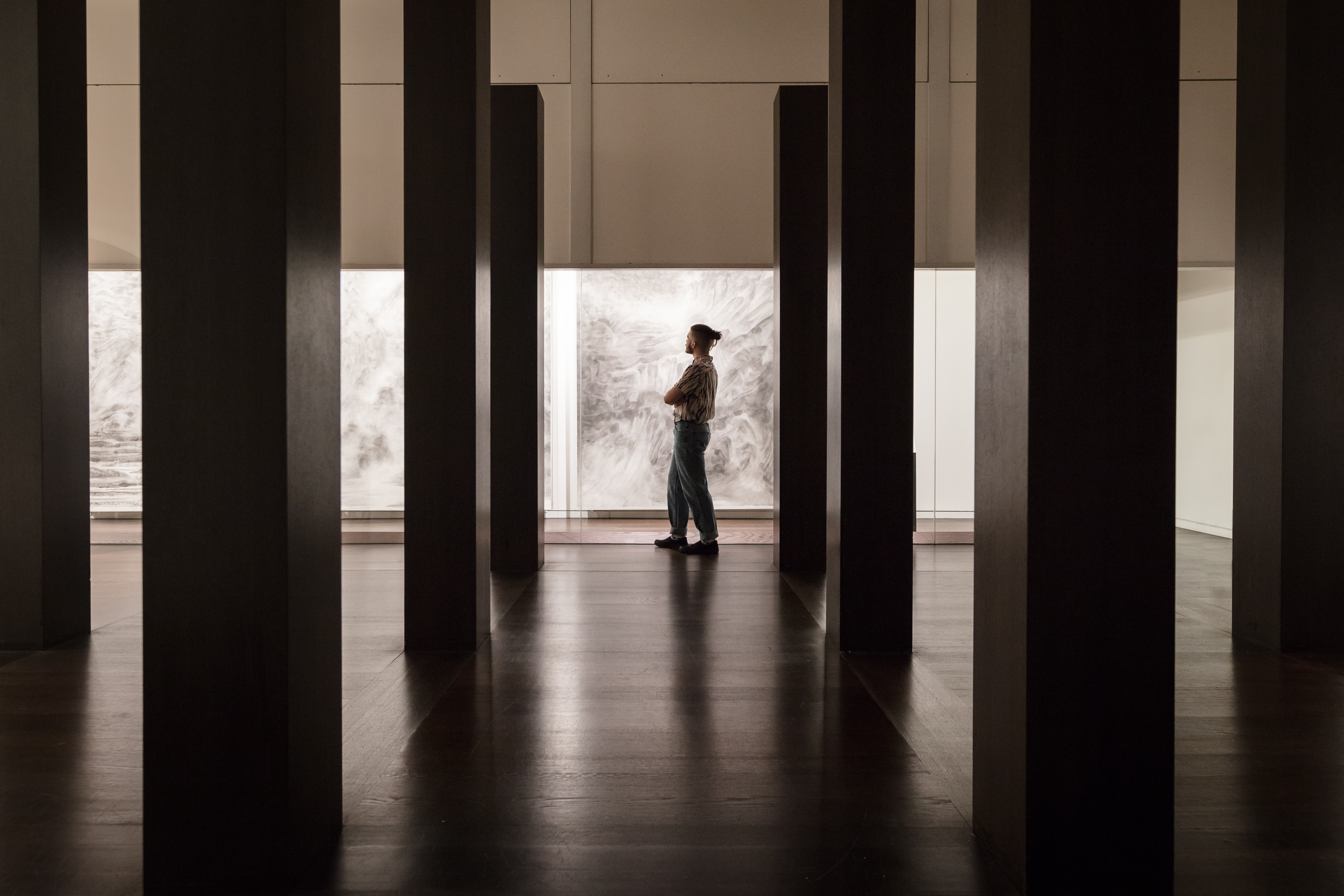 A man stands in a dark gallery, looking at large prints