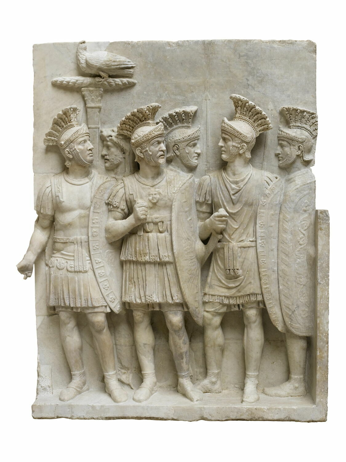 Stone carving of six bare-egged soldiers in helmets carrying shields.