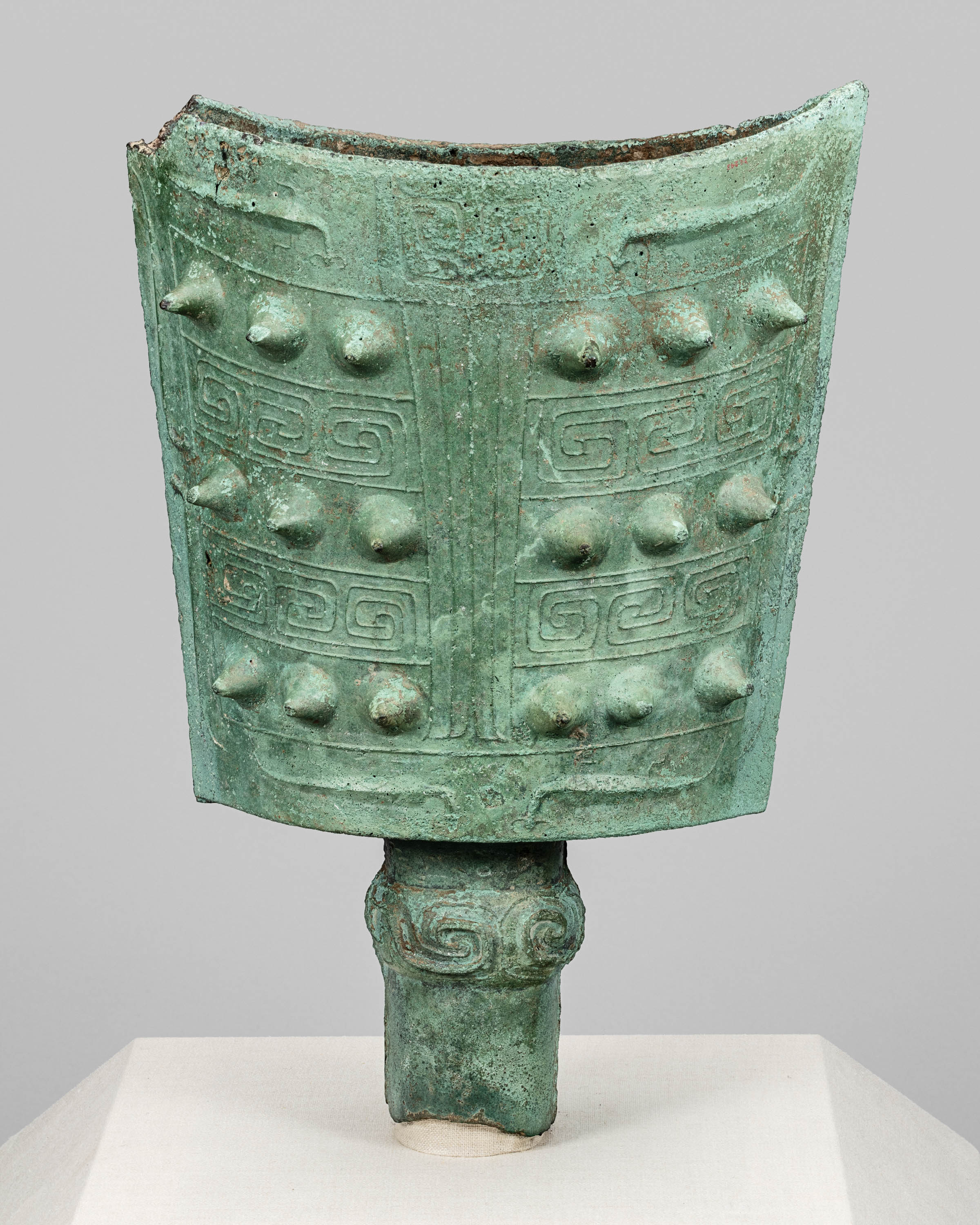 A photo of a bronze bell that is green from age and has decorative ornamentation.
