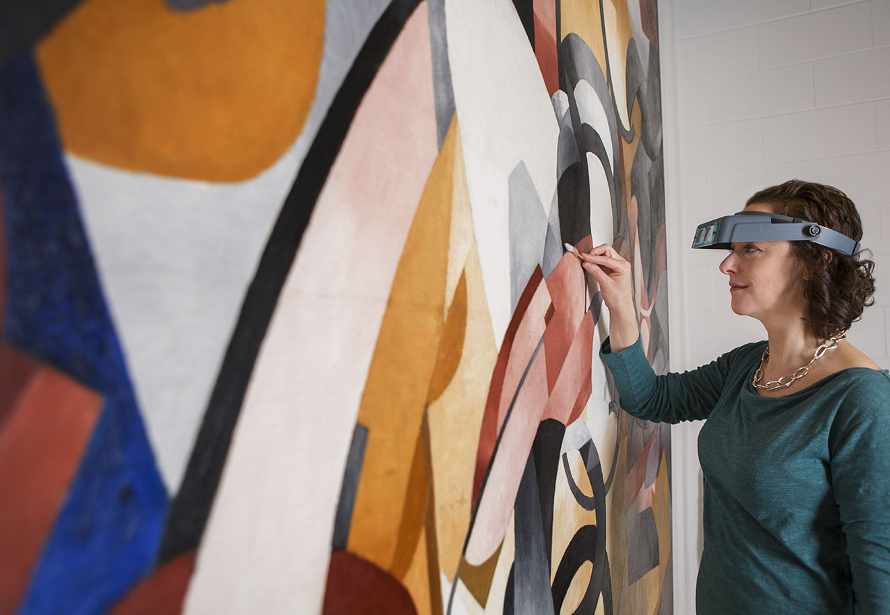 A conservator uses a cotton swab to remove varnish from the surface of an above treating a large abstract canvas by Francis Picabia.