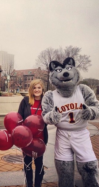 A young Maddie Shearer stands outdoors smiling with a figure in a wolf costume who also wears a Loyola jersey.