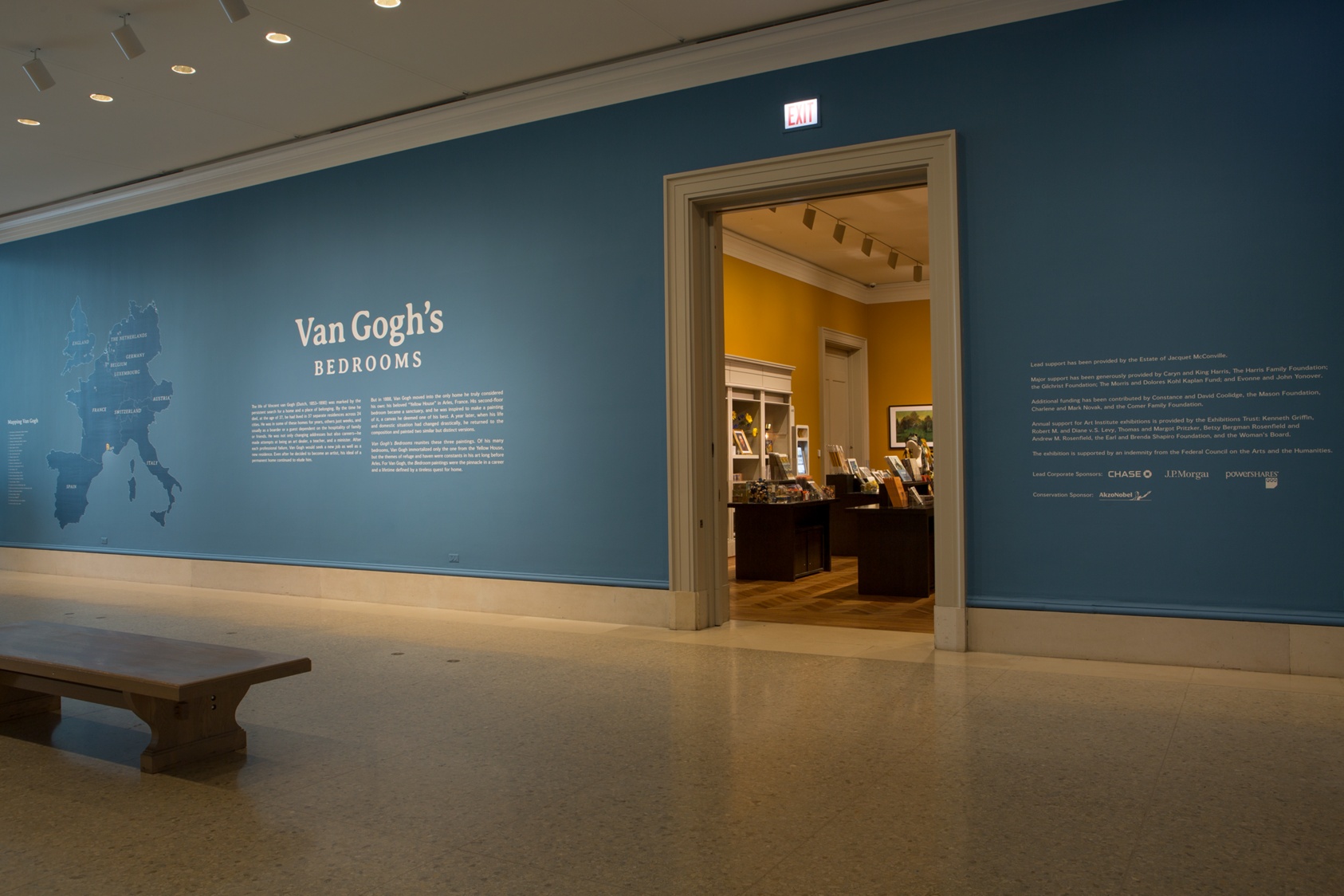 wide, blue wall adjacent to a bench reads "Van Gogh's Bedrooms," a gift shop visible behind an open doorway.