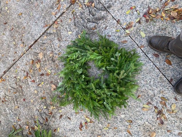 Photo shows a small evergreen wreath set on concrete.