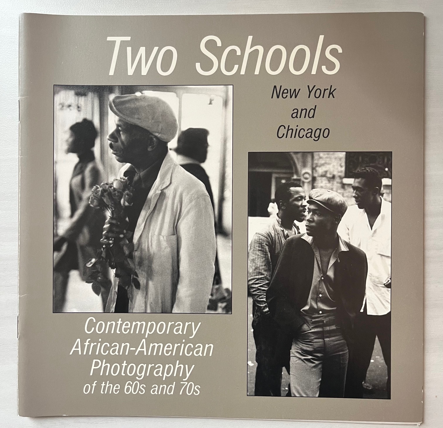 A book cover with two images set over a gray background. The top of the cover says "Two Schools" in large white text, with "New York and Chicago" in smaller dark gray text below. At the bottom of the page, small white text reads "Contemporary African-American Photography of the 60s and 70s." The two images are black and white photographs. The image on the left features a man with a beret and a bouquet of flowers, while the image on the right features three black men speaking to each other and looking off-camera.