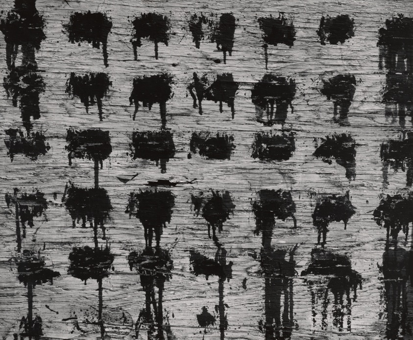 A black-and-white photograph of the surface of a wood panel with thirty-six black dripping paint splotches. The splotches are generally rectangular in shape and follow a grid with seven columns and six rows. The last row is incomplete.