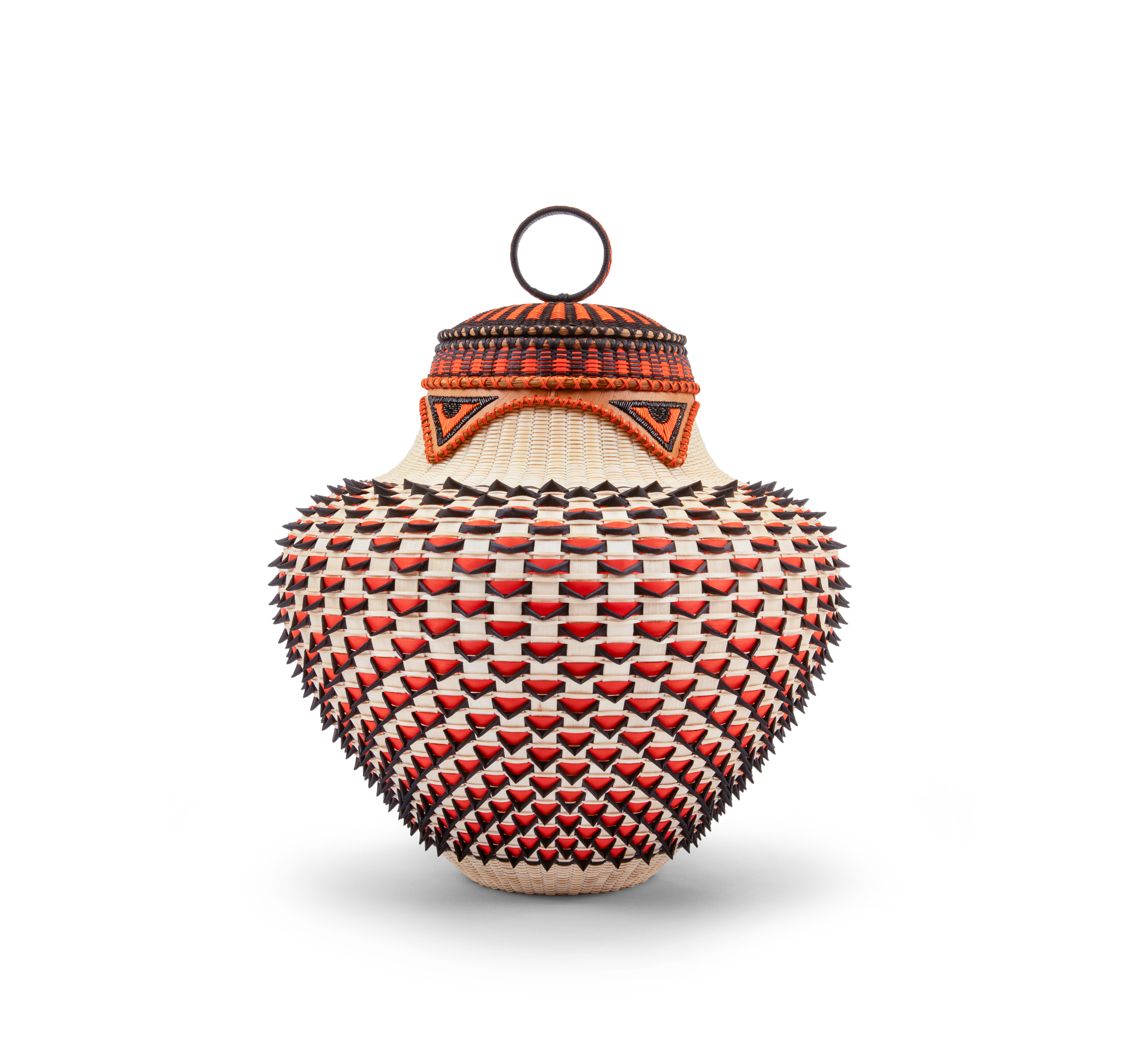 A red, black, and blond wooden basket. Triangular elements in red and black point down around the narrowed neck. The red-and-black striped lid is topped by a a ringed handle.