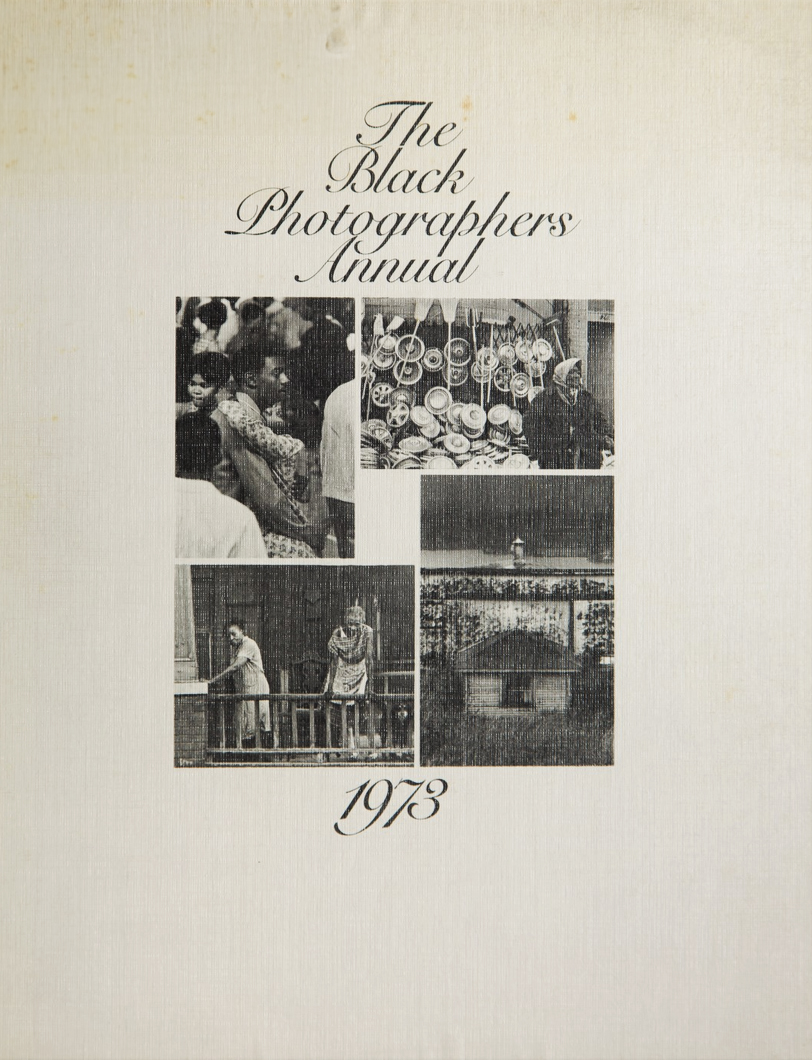 A sheet of paper featuring a two-by-two grid across the middle with four black-and-white photographs: a crowd scene, a display of hats and other goods, two people on a porch, and a small house with a mural behind it. The off-white textured background features "The Black Photographers Annual" in black script at the top center, with the year 1973 in matching script at the bottom center.