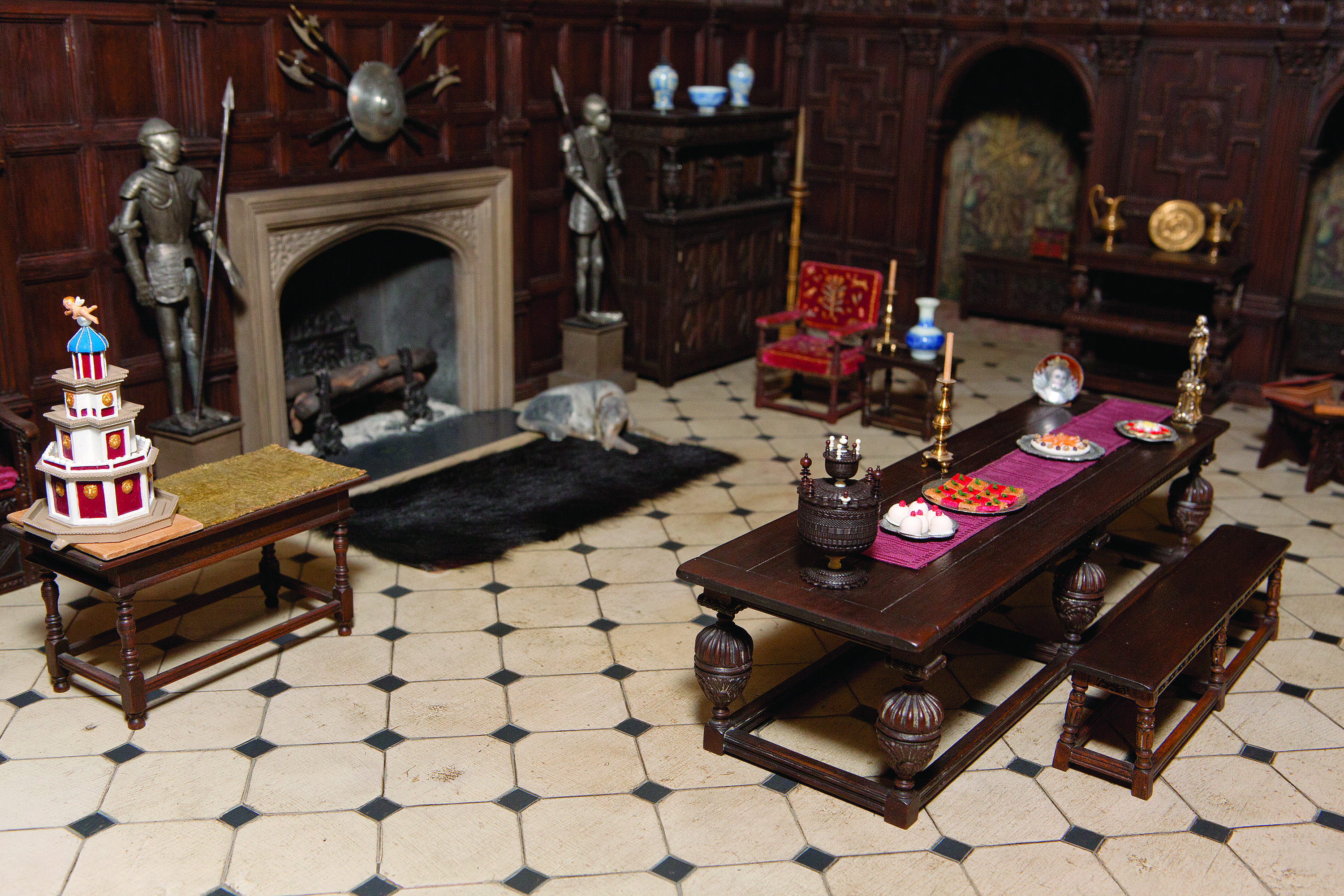 A photo of the wood-paneled great room of a Tudor-style miniature Thorne Room, decorated for the holidays with festive food and drink on a long table.