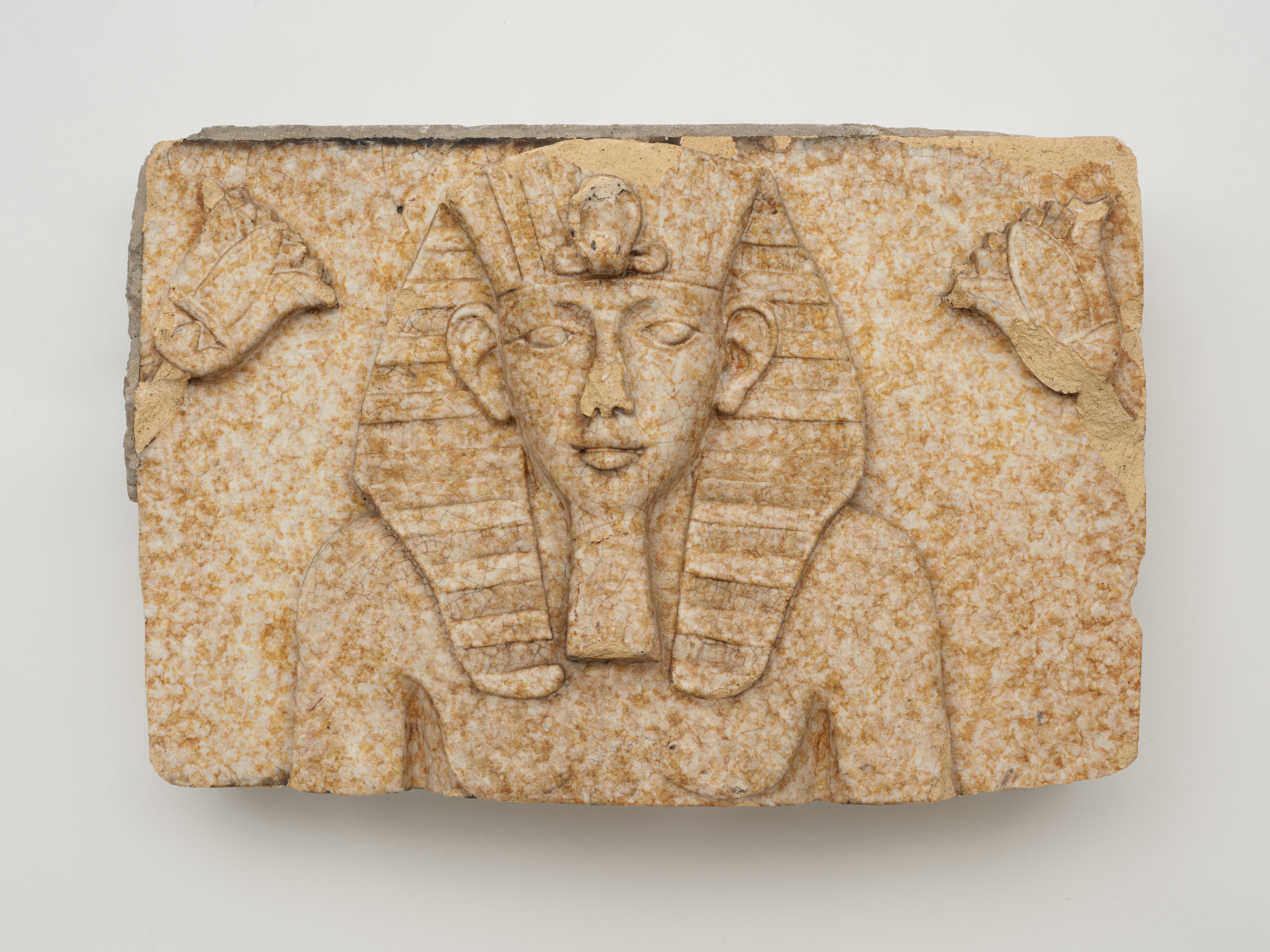 A carving in tan-and-white stone of the upper body of a pharaoh wearing an elaborate headdress