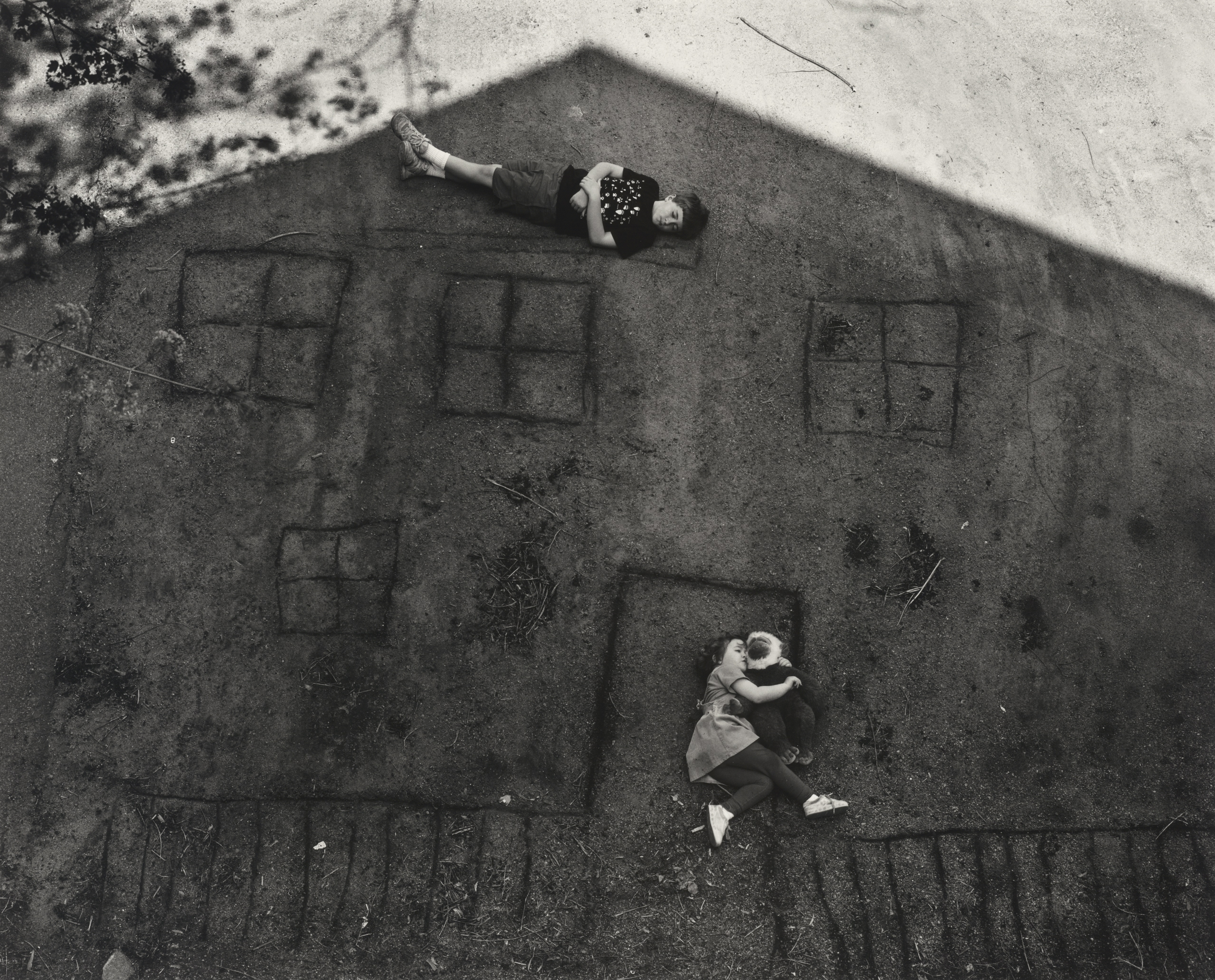 Two children lay in the shadow of their house on the ground