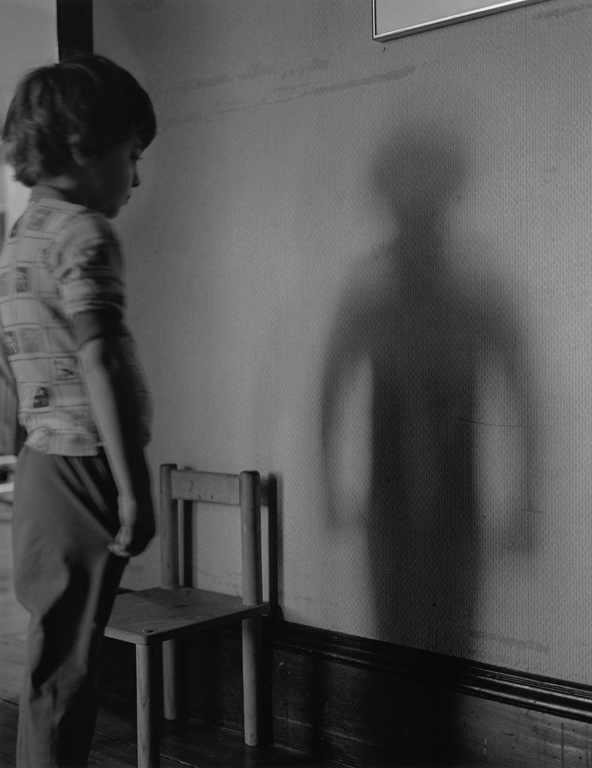 Little boy looks at his shadow on a wall