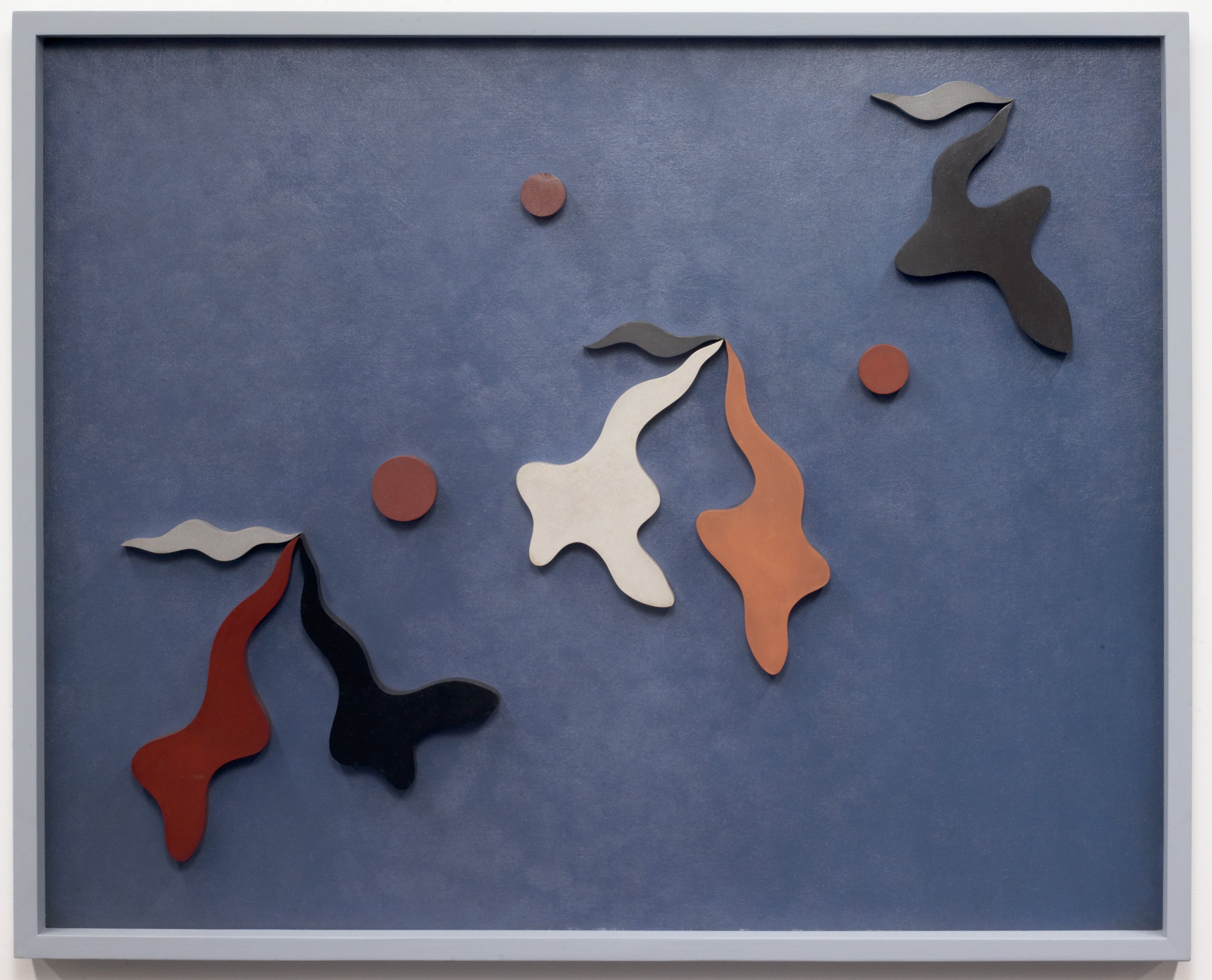 Relief sculpture of abstract, blob-like shapes and circles in red, white, and black/dark blue on a grey-blue background.