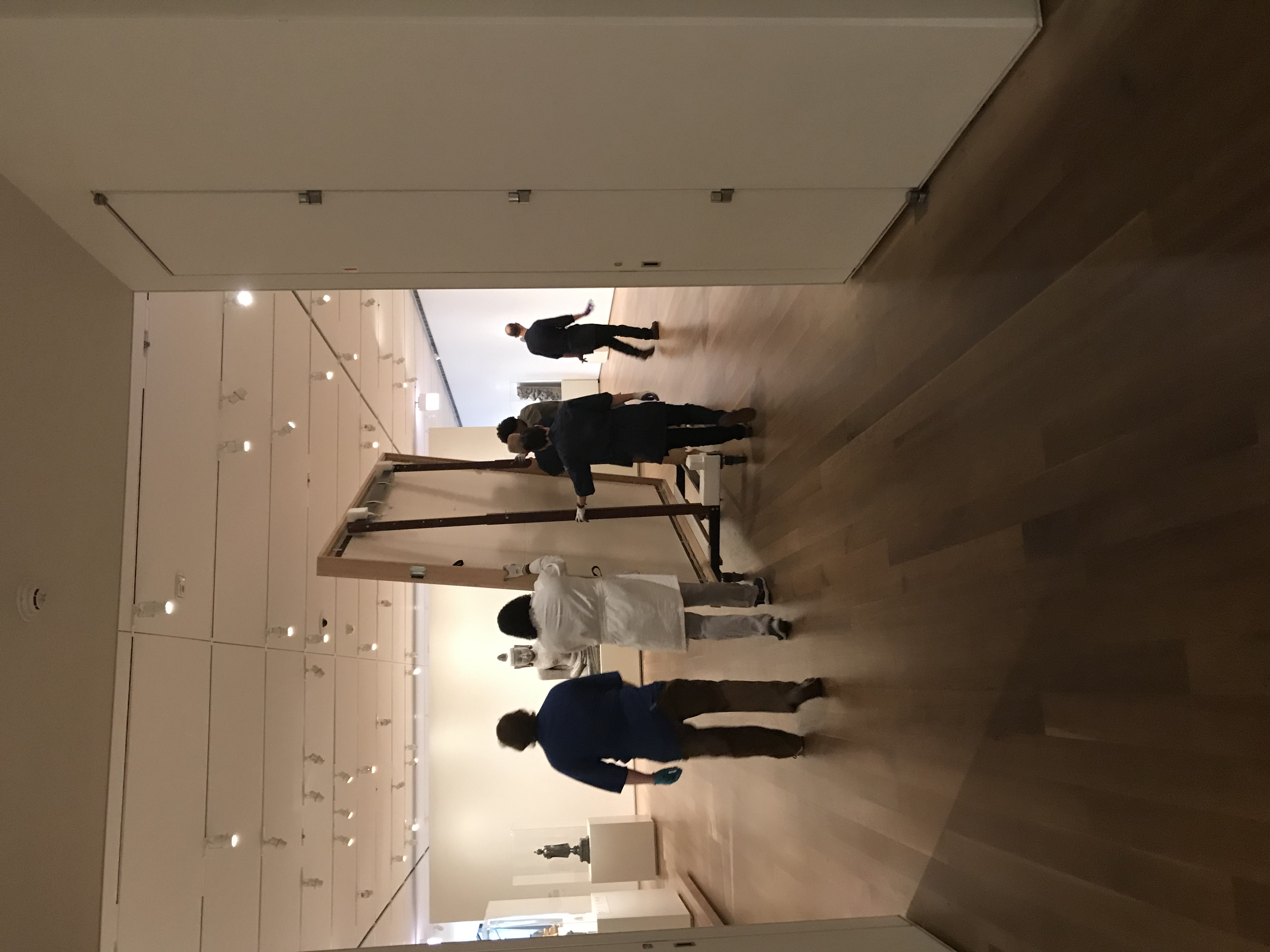 Several art handlers move a large canvas on a wheeled cart through the museum galleries.