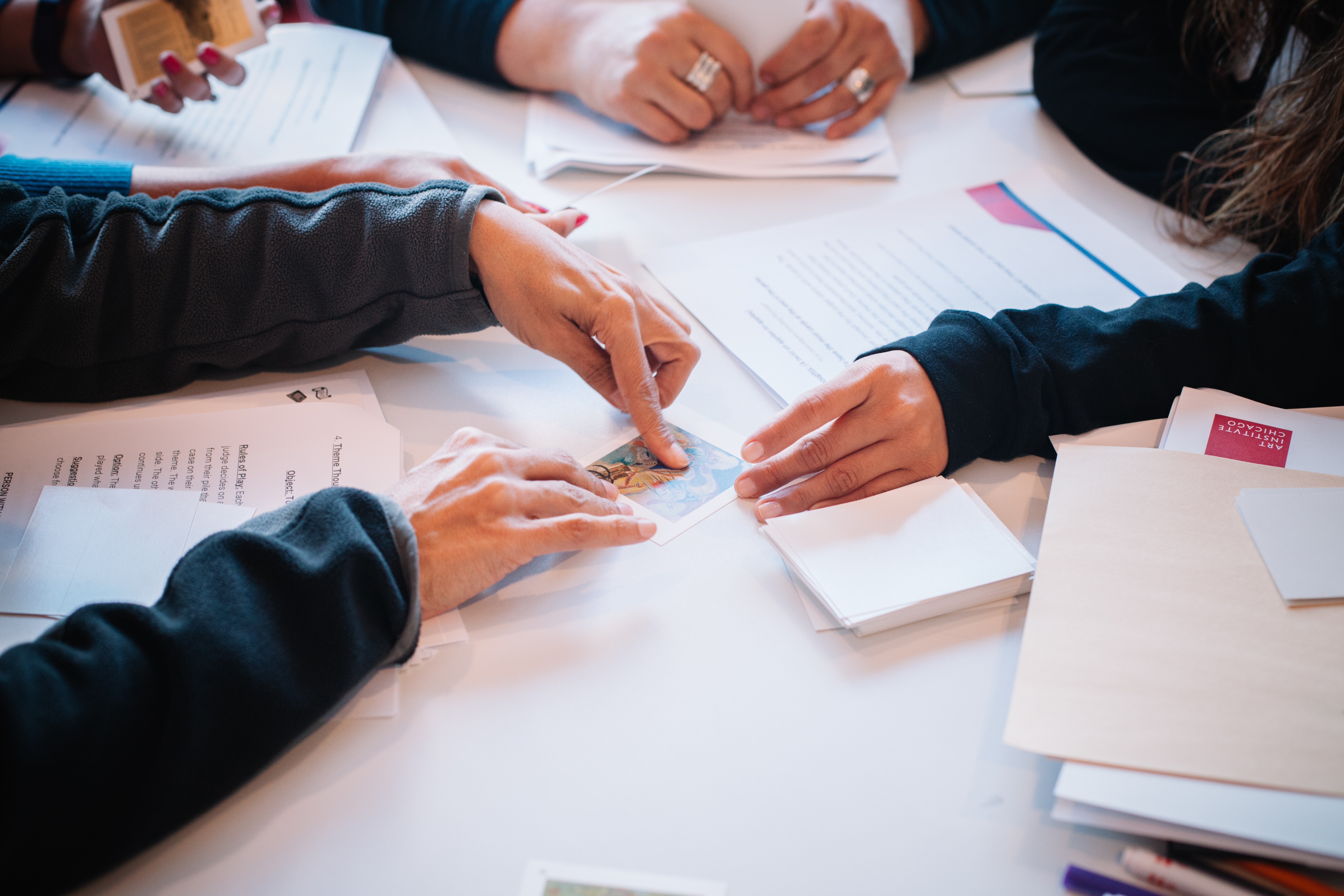 Photograph of people's hands holding and pointing to something on a piece of paper.