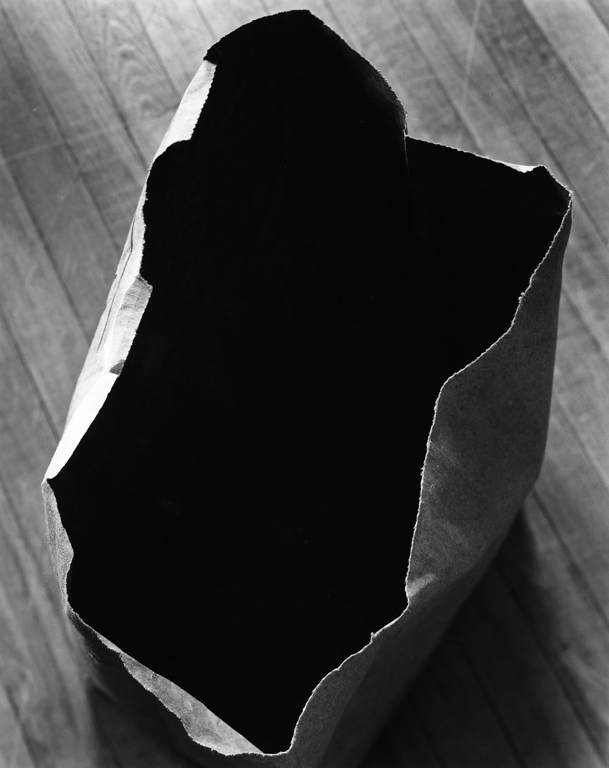 An empty paper bag, photographed from the top, seems to contain a dark void.