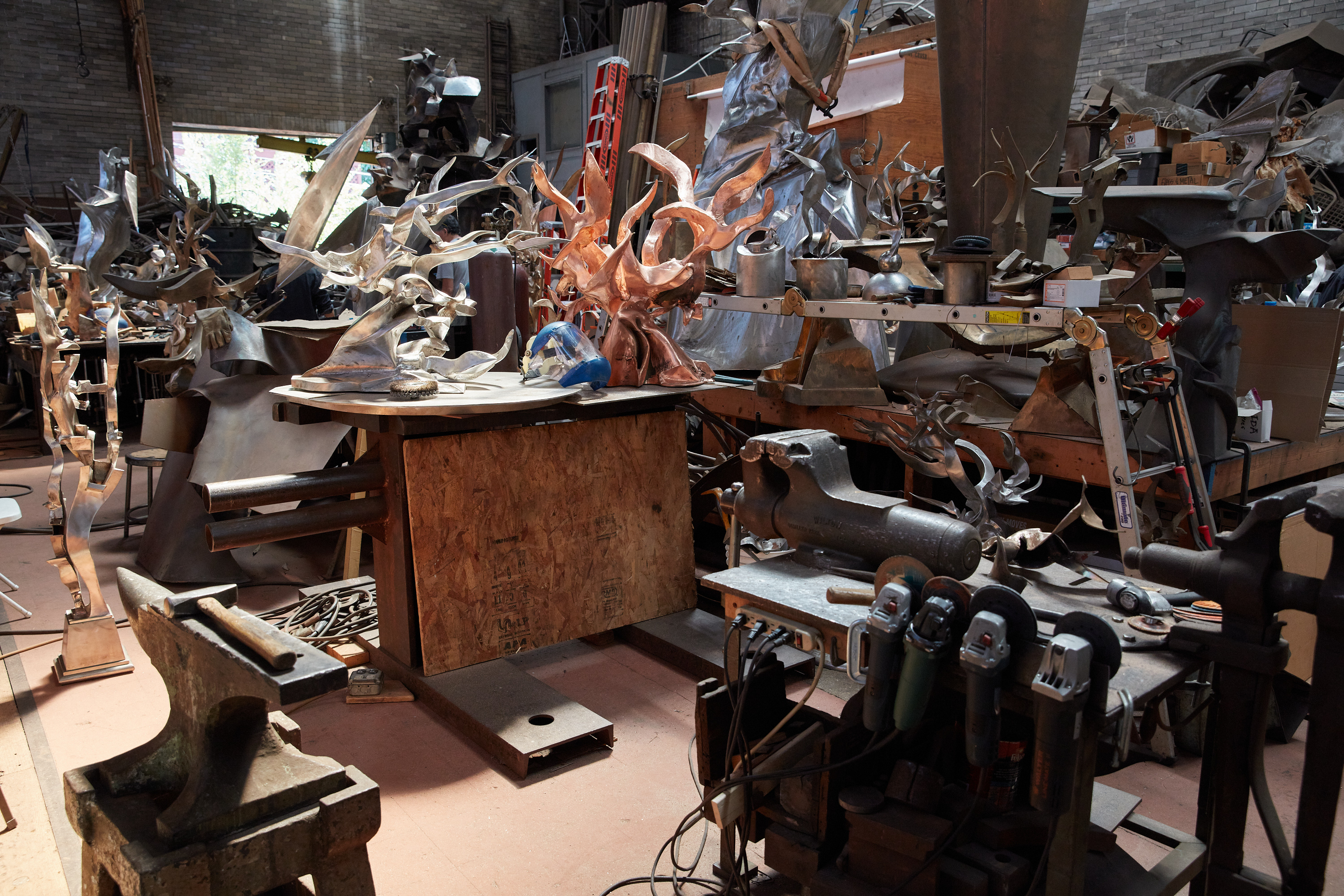 A cluttered studio workspace filled only with sculptural works and tools, including numerous power tools and an anvil.