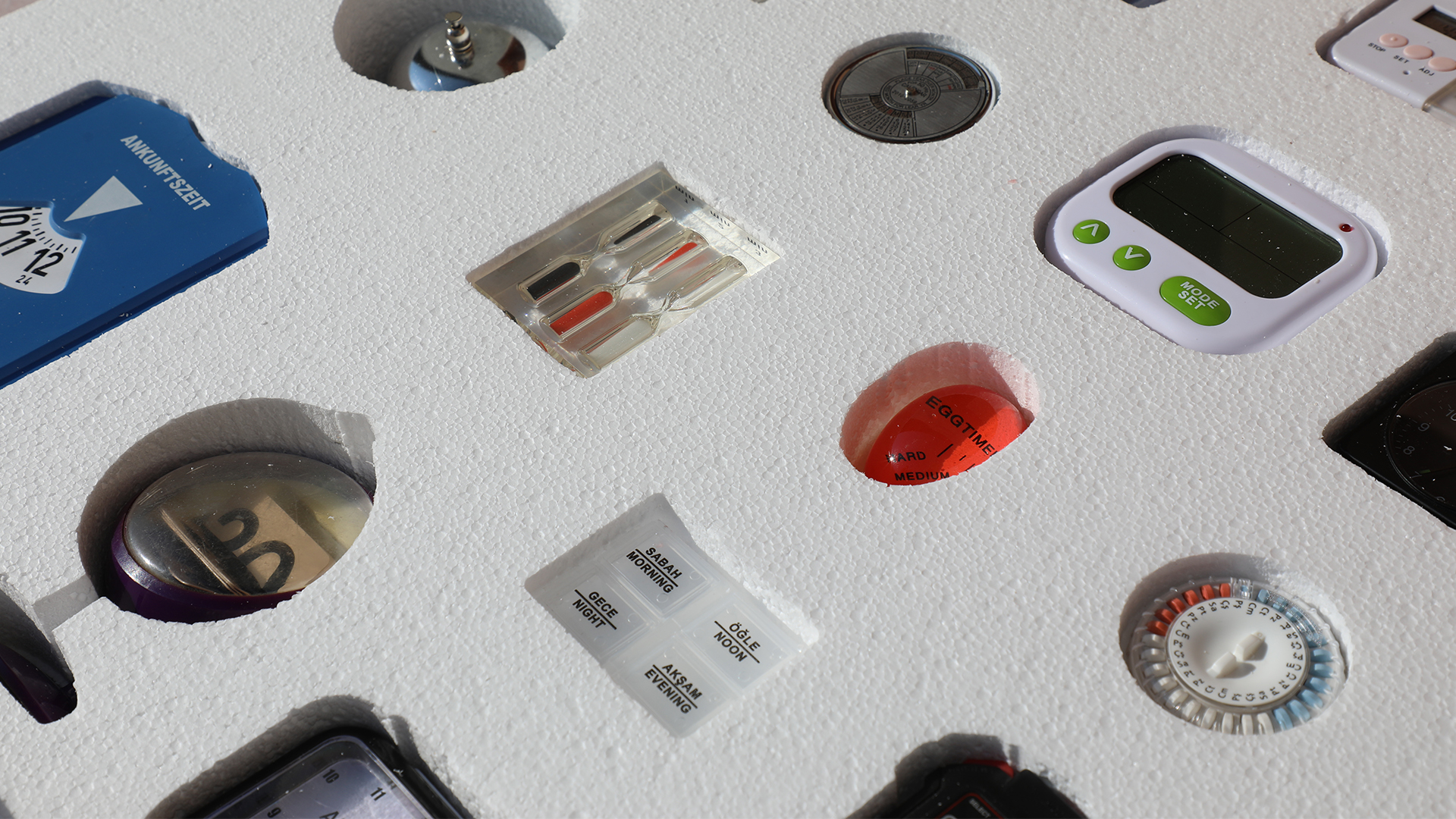 Close-up photo of different types of timers and clocks resting in a sheet of styrofoam.